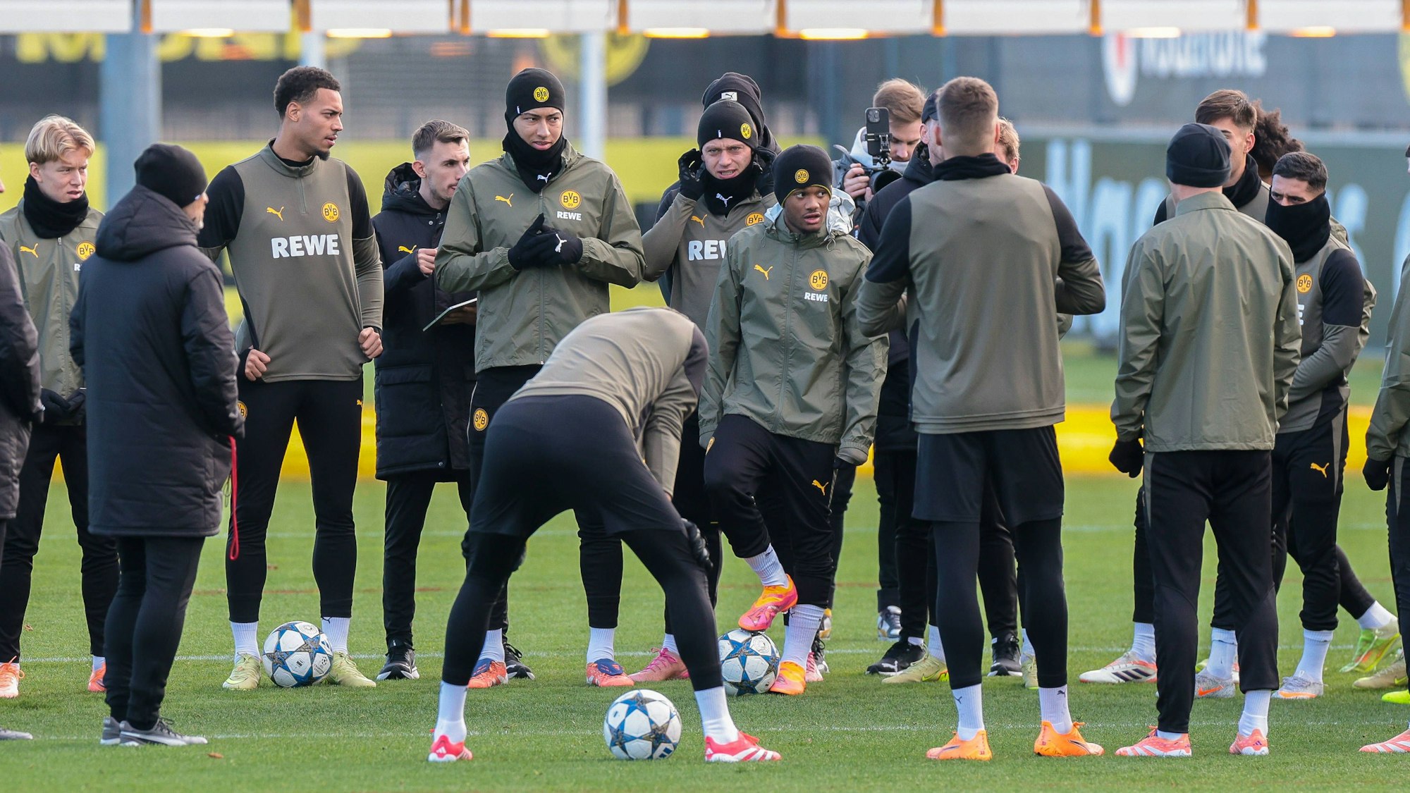 Julien Duranville und Fußballspieler in Trainingskleidung stehen auf einem Rasenplatz mit Bällen