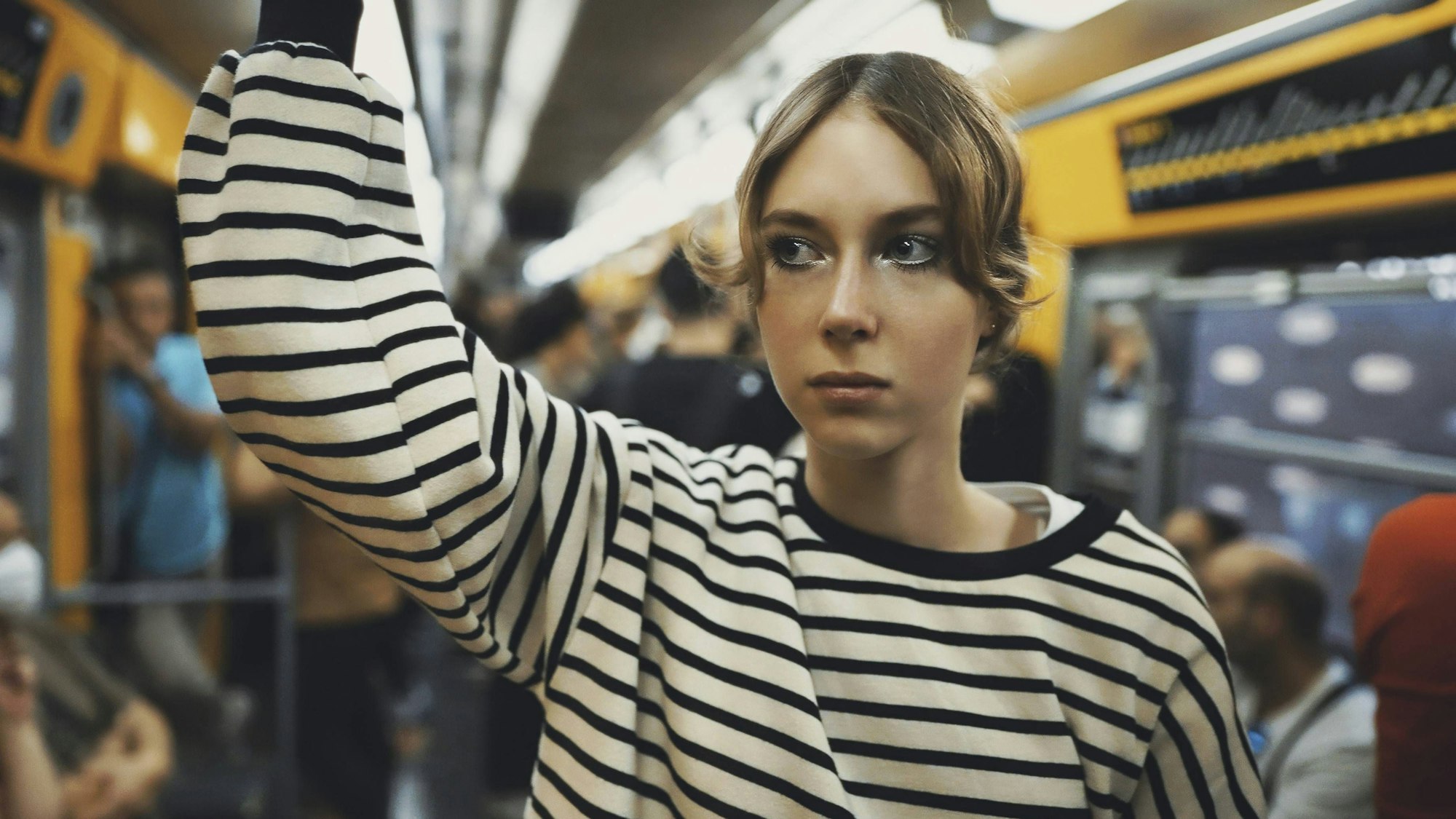 Mädchen in gestreiftem Oberteil hält sich in einer U-Bahn fest und blickt nach rechts