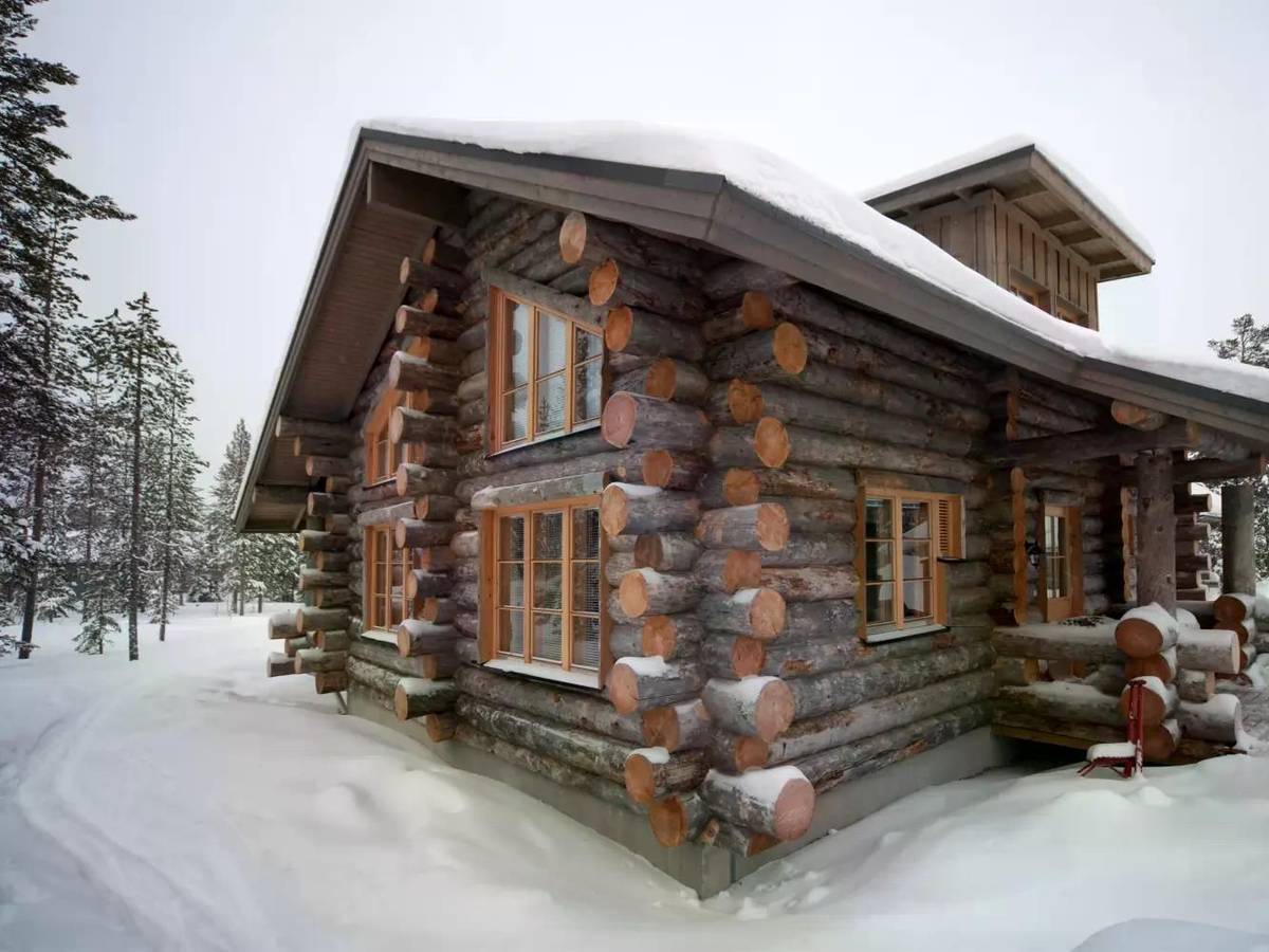 Das Bild zeigt eine gemütliche Hütte im verschneiten Winterwald in Finnisch-Lappland