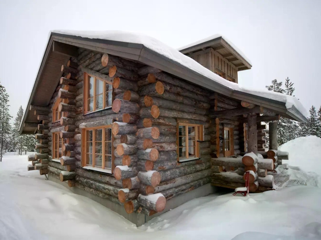 Das Bild zeigt eine gemütliche Hütte im verschneiten Winterwald in Finnisch-Lappland