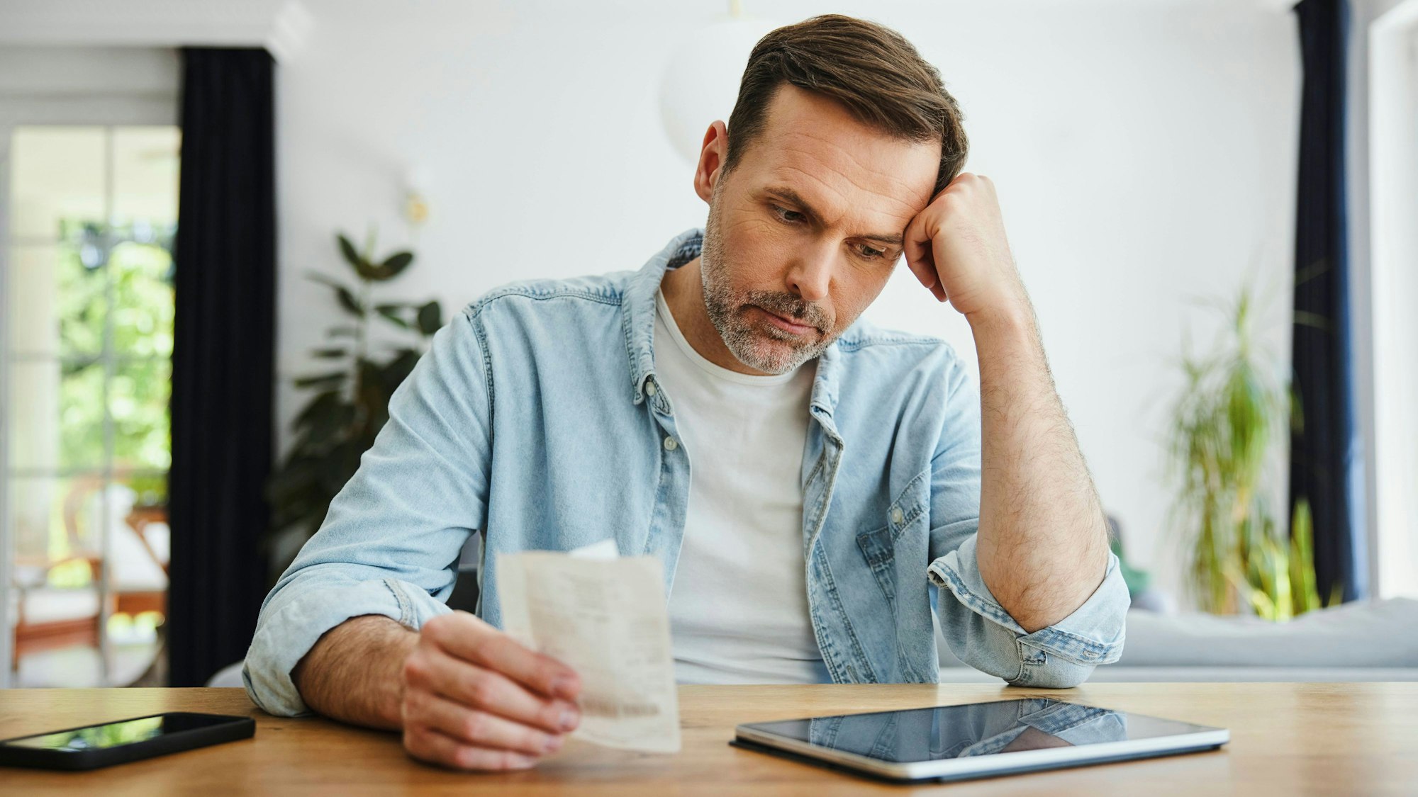 Ein unglücklicher Mann schaut auf eine Rechnung und sein Smartphone.