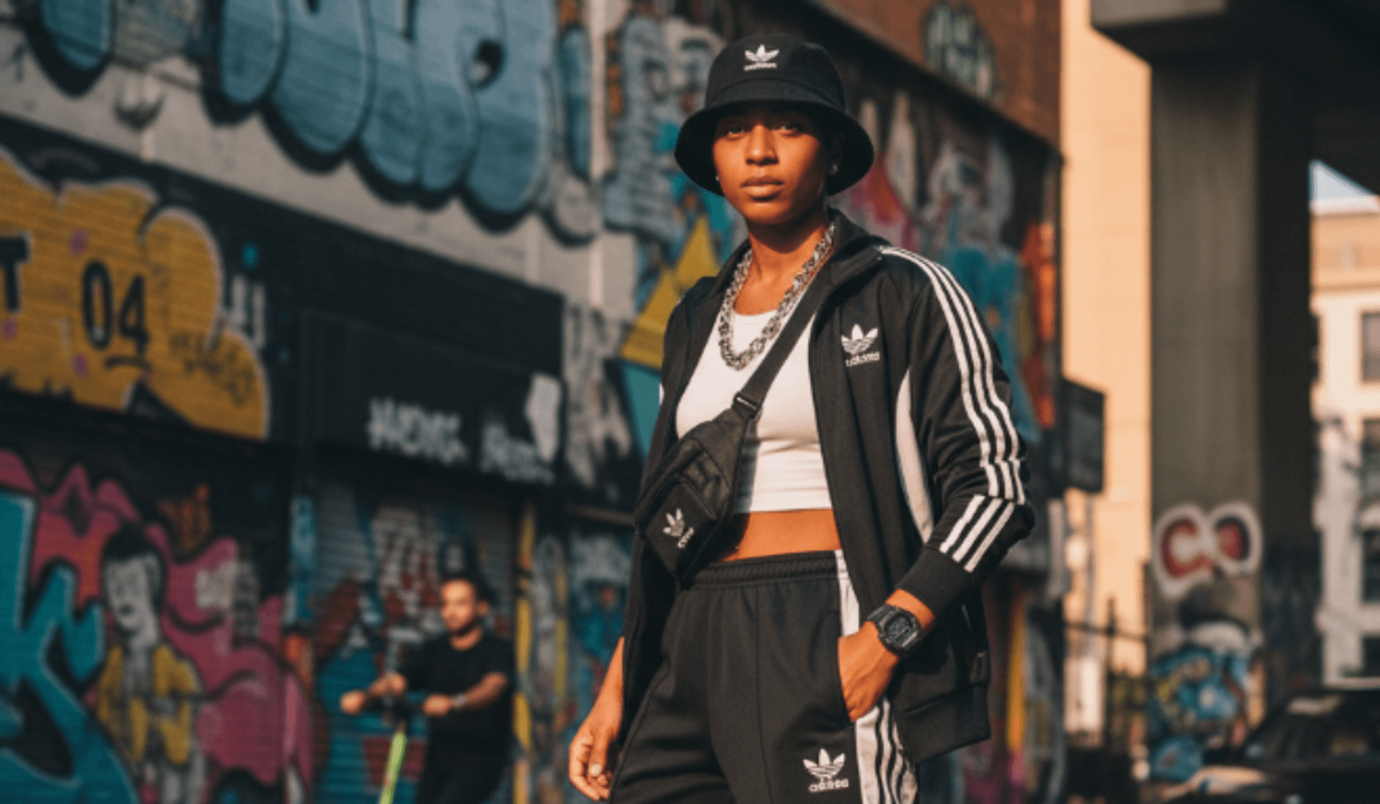 Frau steht mit adidas Freizeitkleidung Trainingsanzug vor einer Mauer mit Graffiti.