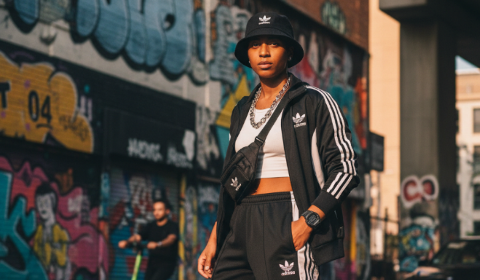 Frau steht mit adidas Freizeitkleidung Trainingsanzug vor einer Mauer mit Graffiti.