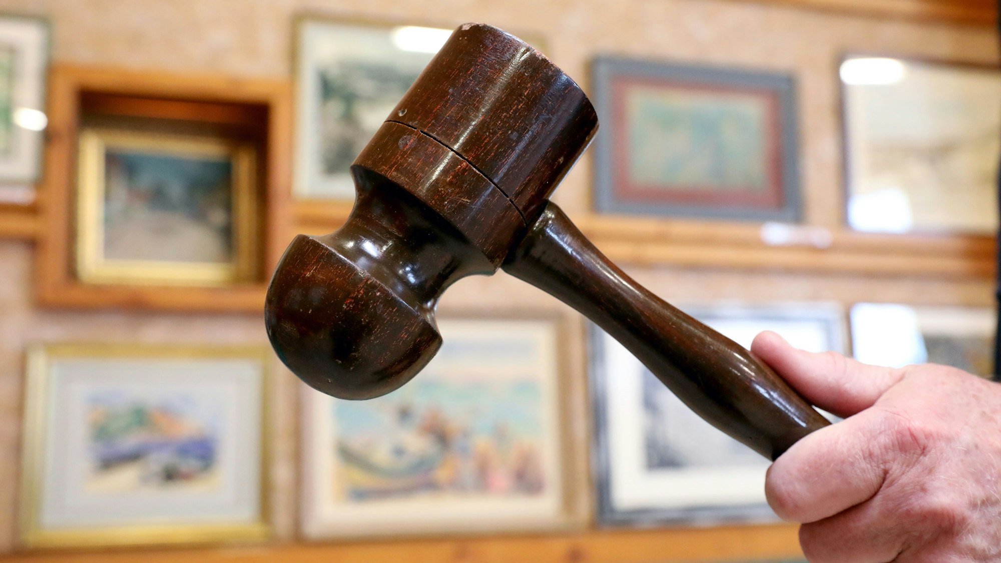 Die Hand eines Auktionators hebt einen Auktionshammer.