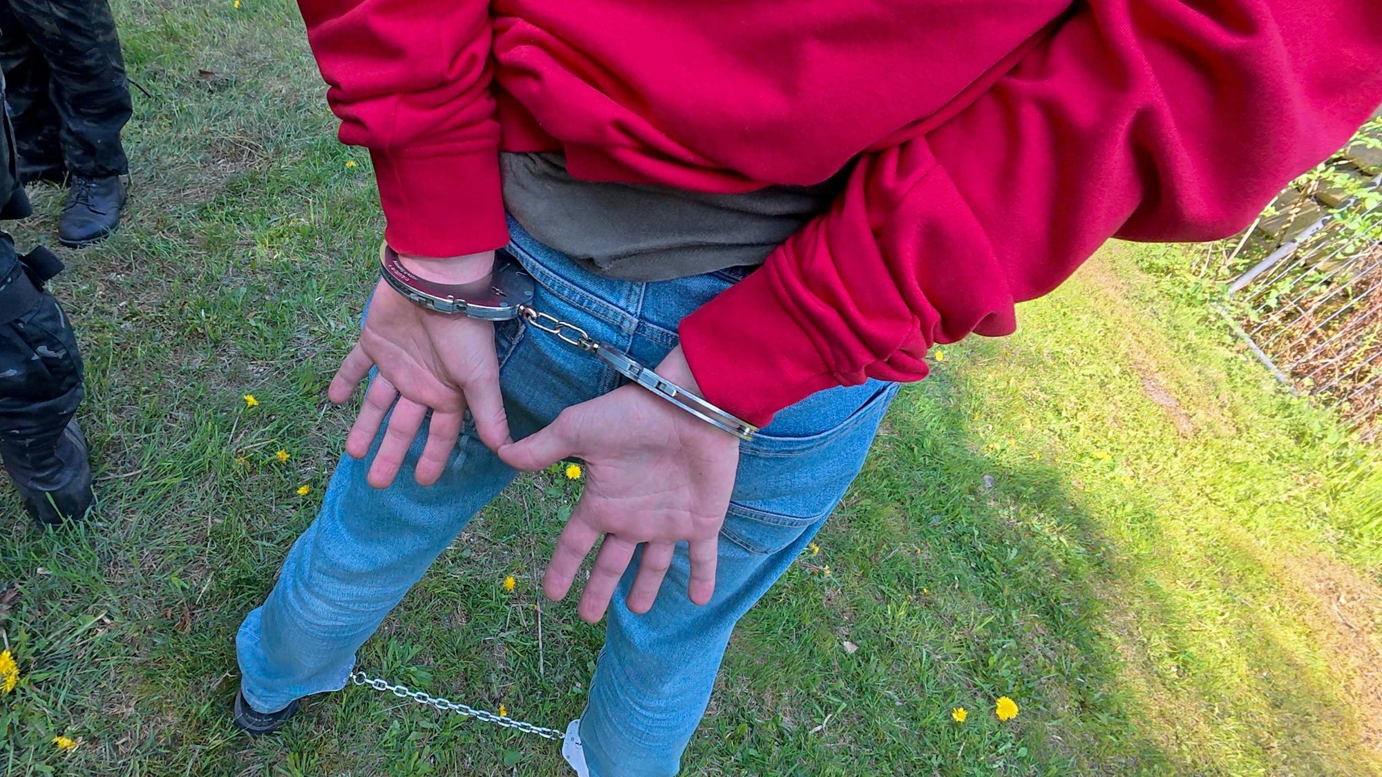 Eine Person in rotem Hoodie und Jeans, von der Polizei auf einer Wiese festgenommen