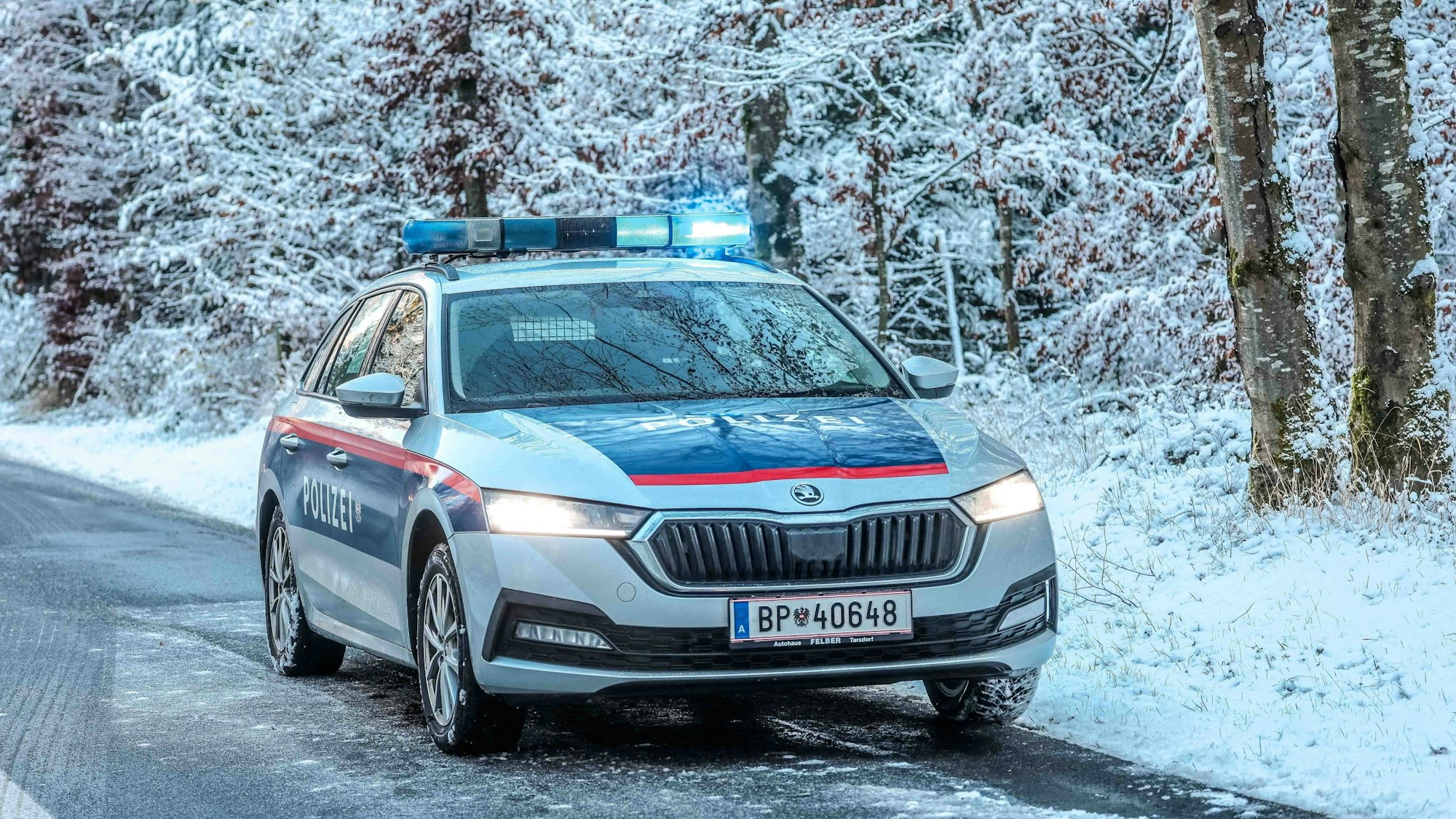 Österreichisches Polizeiauto mit Blaulicht bei einem Einsatz auf schneebedeckter Straße im Wald