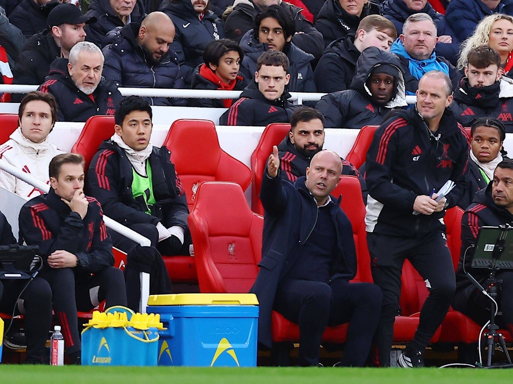 Mehrere Männer sitzen auf der Ersatzbank eines Fußballspiels, einer davon gestikuliert.