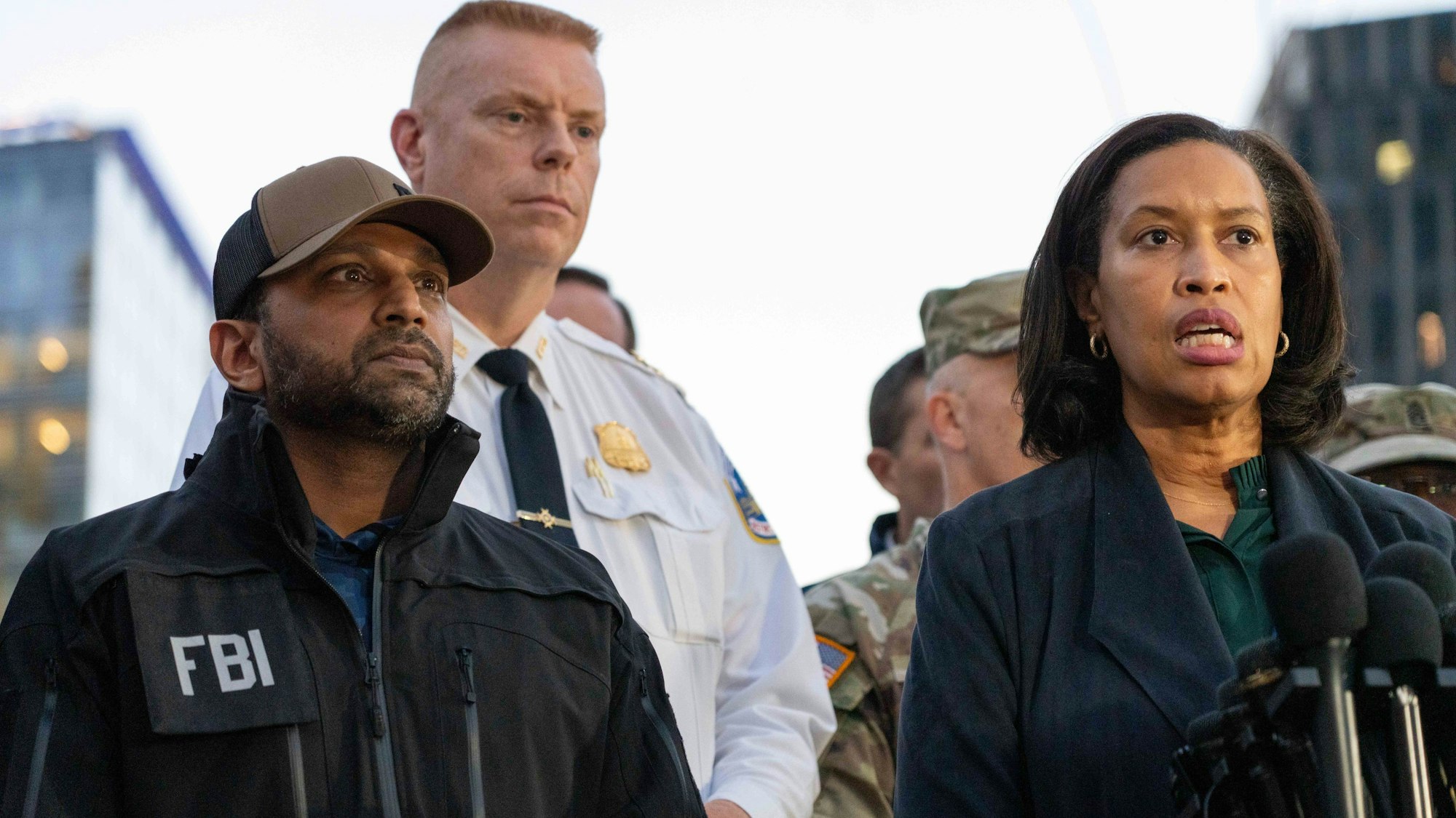 Eine Frau spricht in ein Mikro, sie steht neben einem Mann, auf dessen Jacke FBI steht.