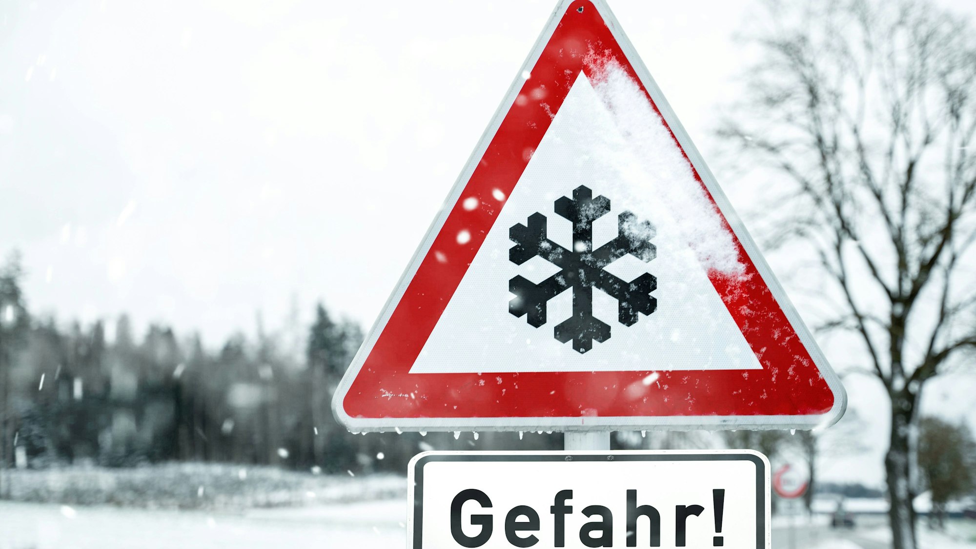Ein Warnschild mit Schneeflocke und „Gefahr!“ im verschneiten Winter.