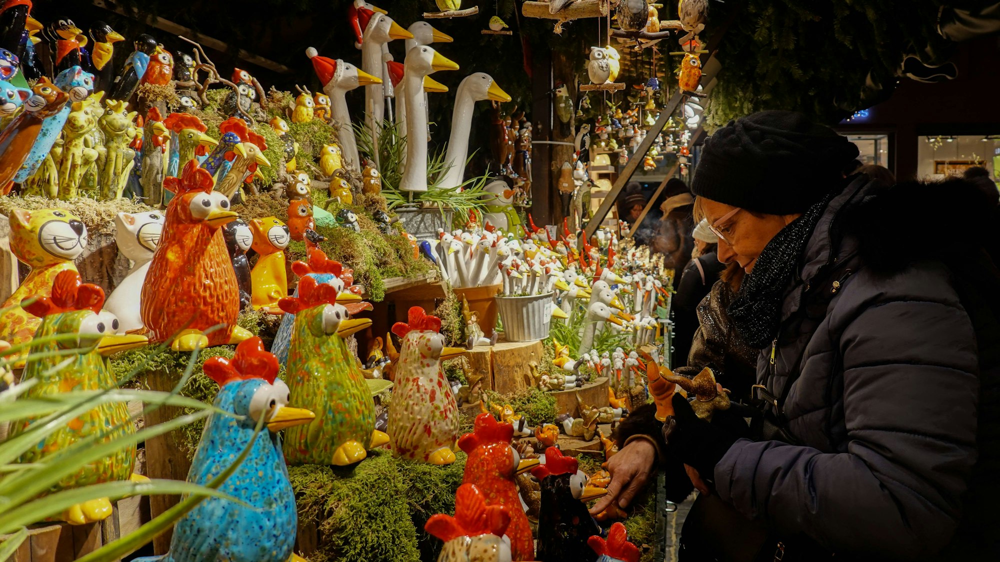 Eine Person betrachtet bunte Keramikfiguren an einem Stand auf dem Augsburger Christkindlesmarkt