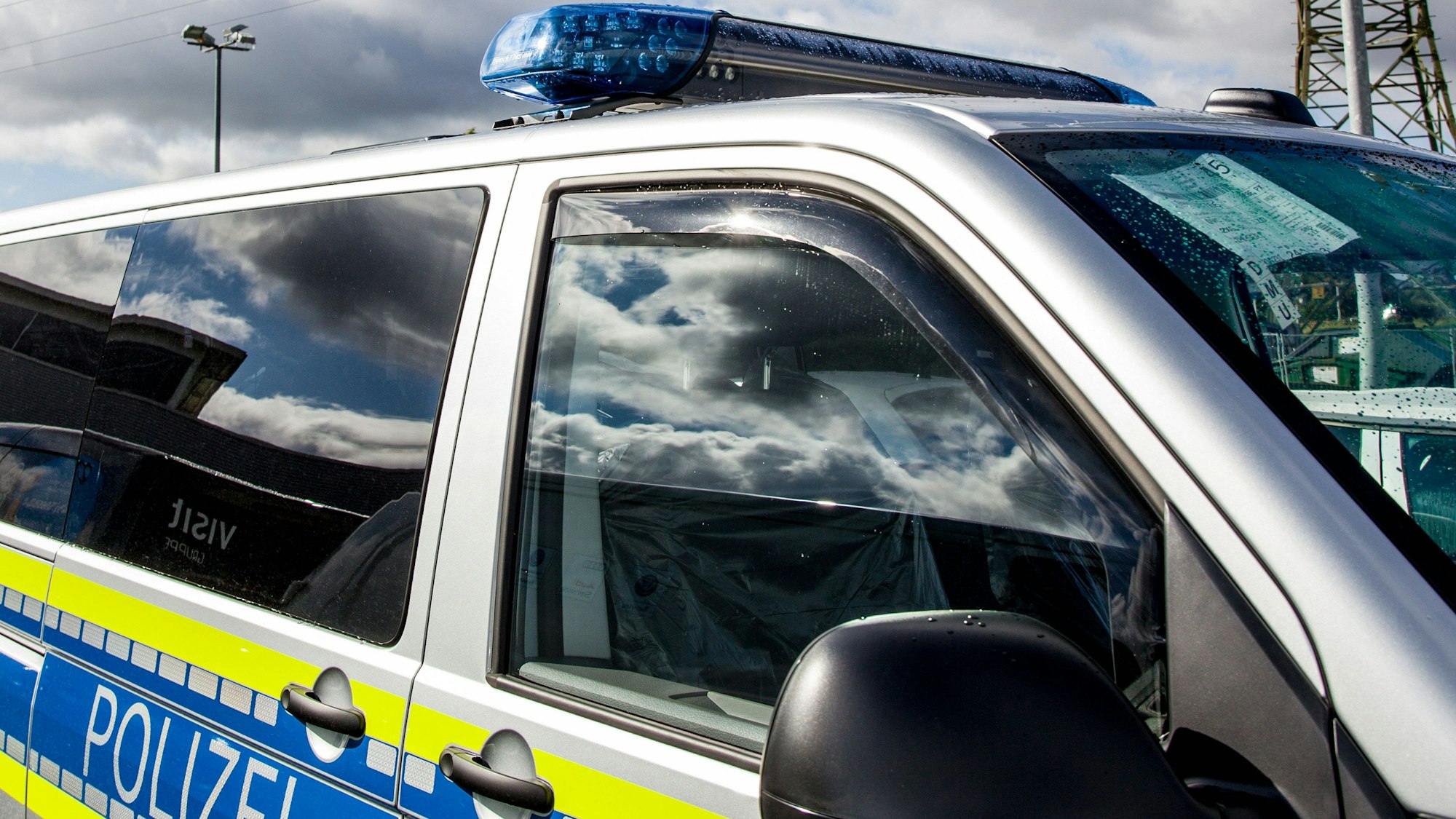Nahaufnahme eines deutschen Polizeifahrzeugs mit Blaulicht, Wassertropfen und Reflexionen am Seitenfenster