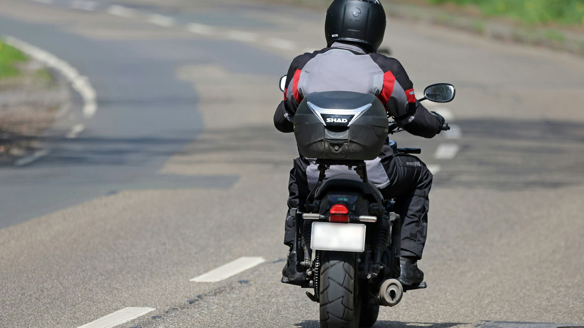 Rückansicht eines Motorradfahrers in Schutzkleidung auf einem Motorrad mit Topcase auf der Straße