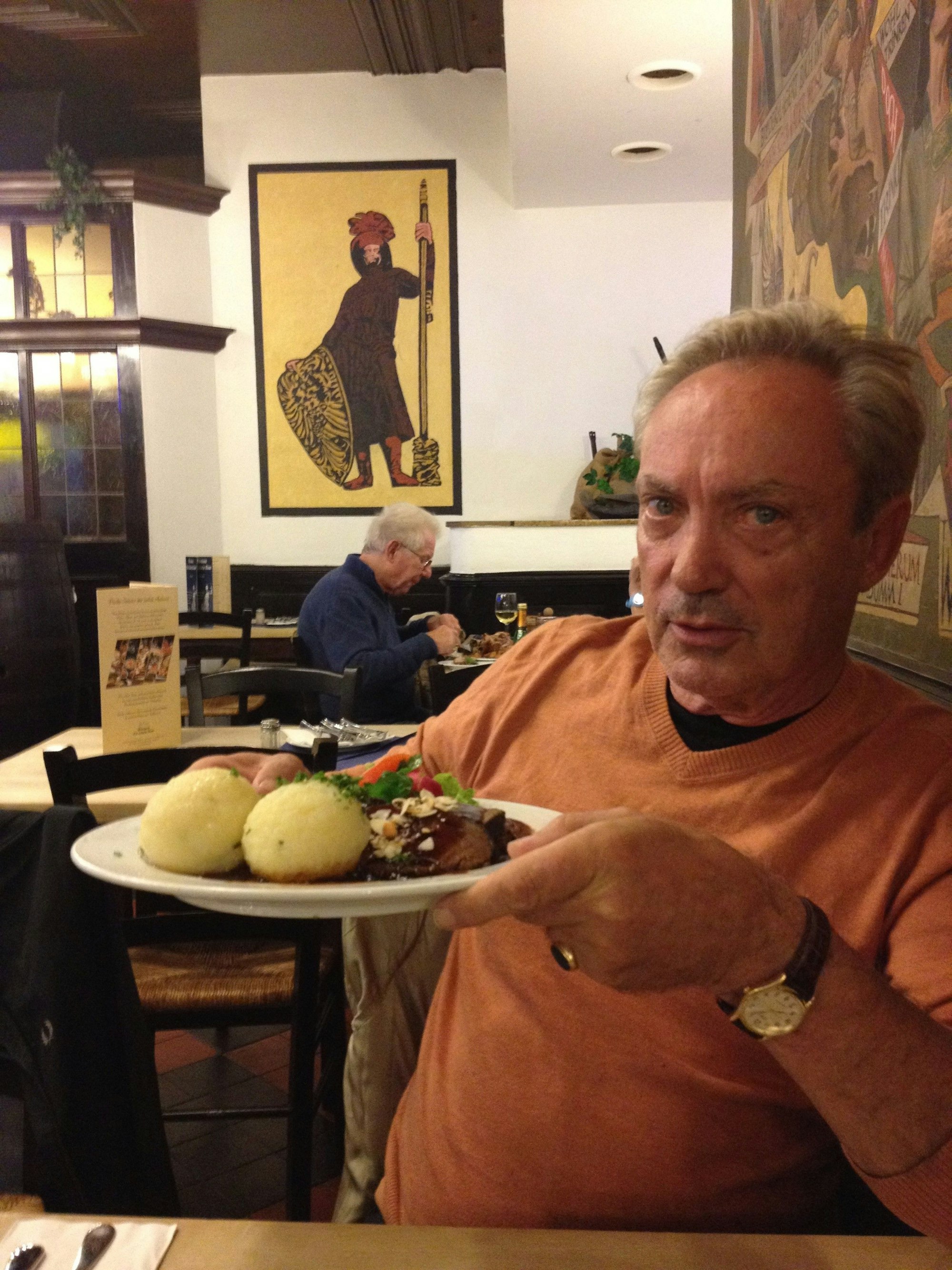 Udo Kier hält im Brauhaus einen Essensteller in die Kamera.