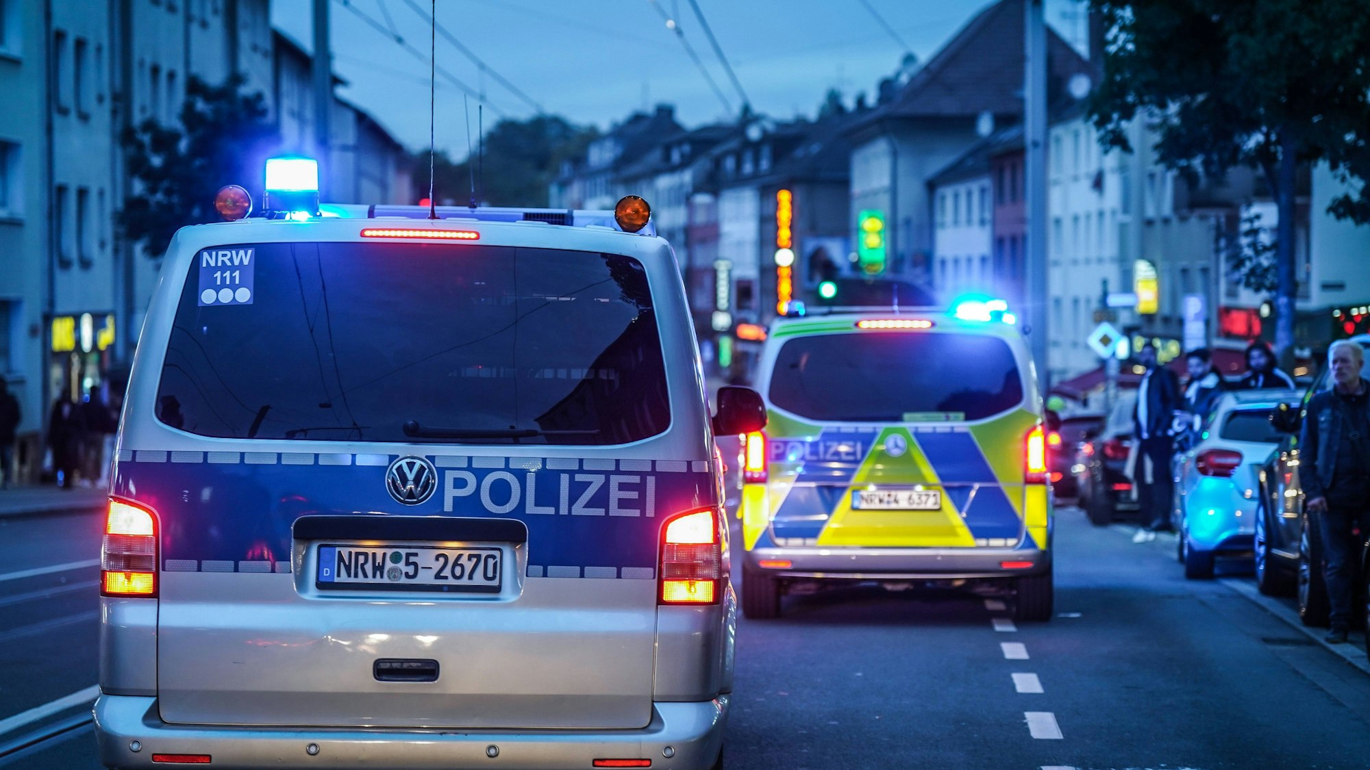 Zwei deutsche Polizeiautos mit Blaulicht stehen abends auf einer Stadtstraße