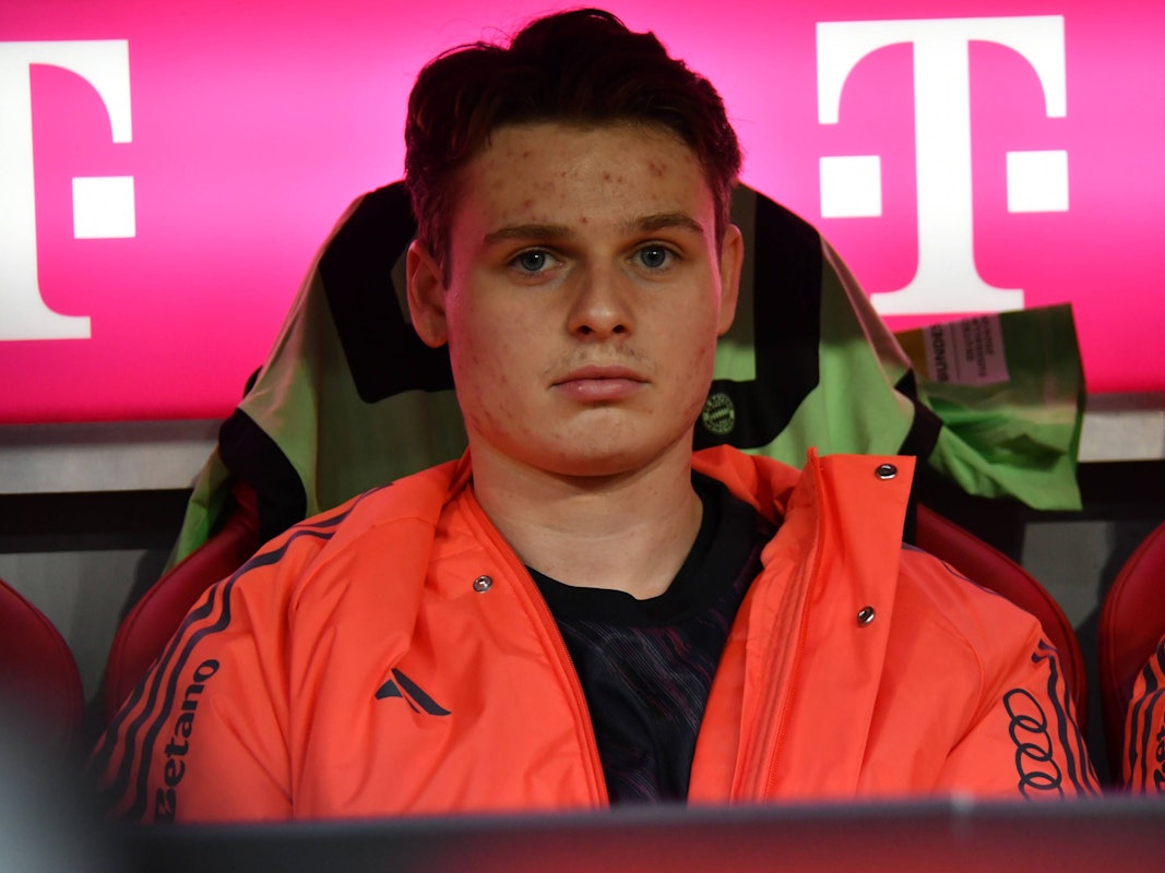 Jonas Urbig sitzt auf der Ersatzbank und guckt ernst in die Kamera.