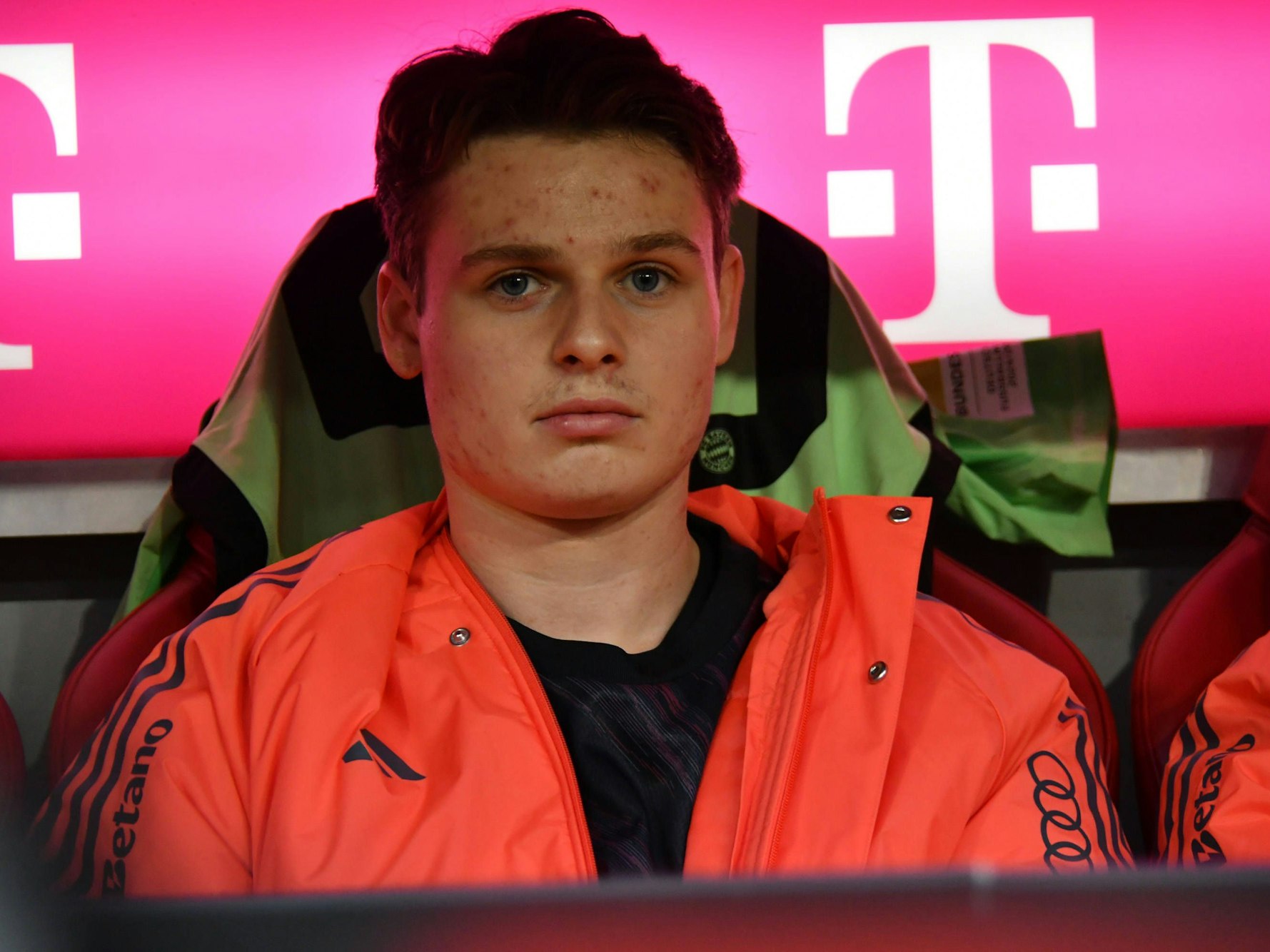 Jonas Urbig sitzt auf der Ersatzbank und guckt ernst in die Kamera.