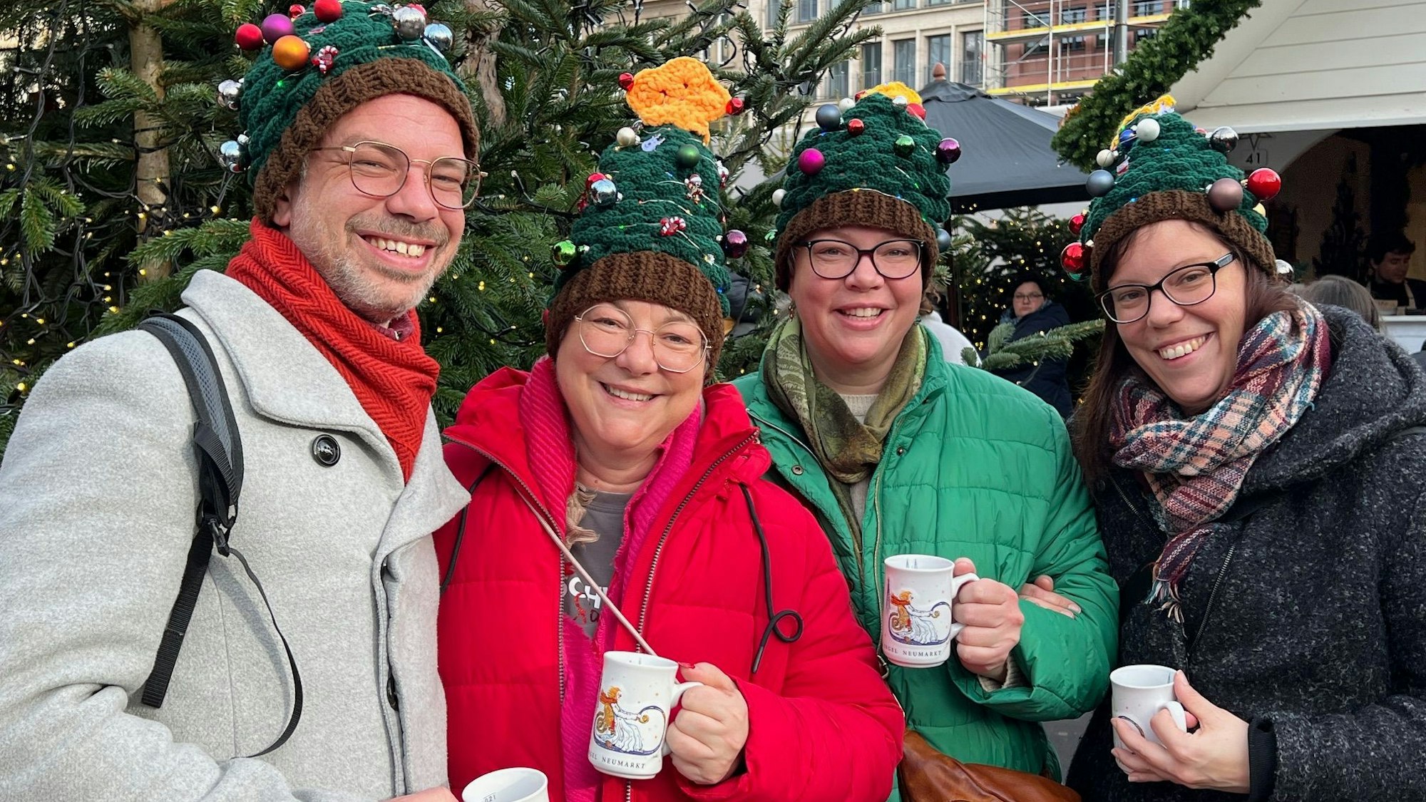 Vier Geschwister posieren mit leuchtenden Tannenbaummützen auf dem Weihnachtsmarkt.