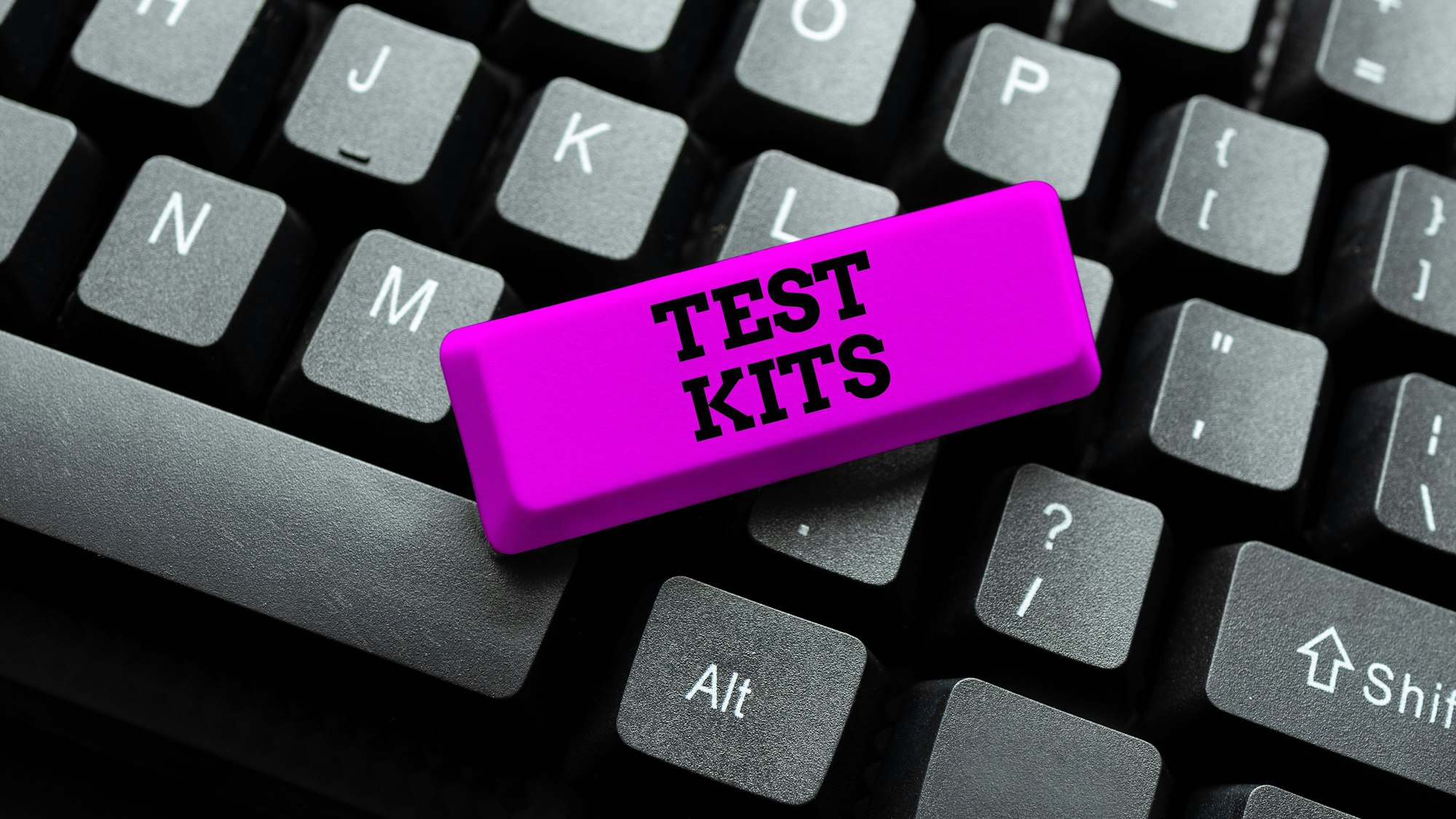 Nahaufnahme einer schwarzen Tastatur mit einer auffälligen magenta Taste, die "TEST KITS" anzeigt