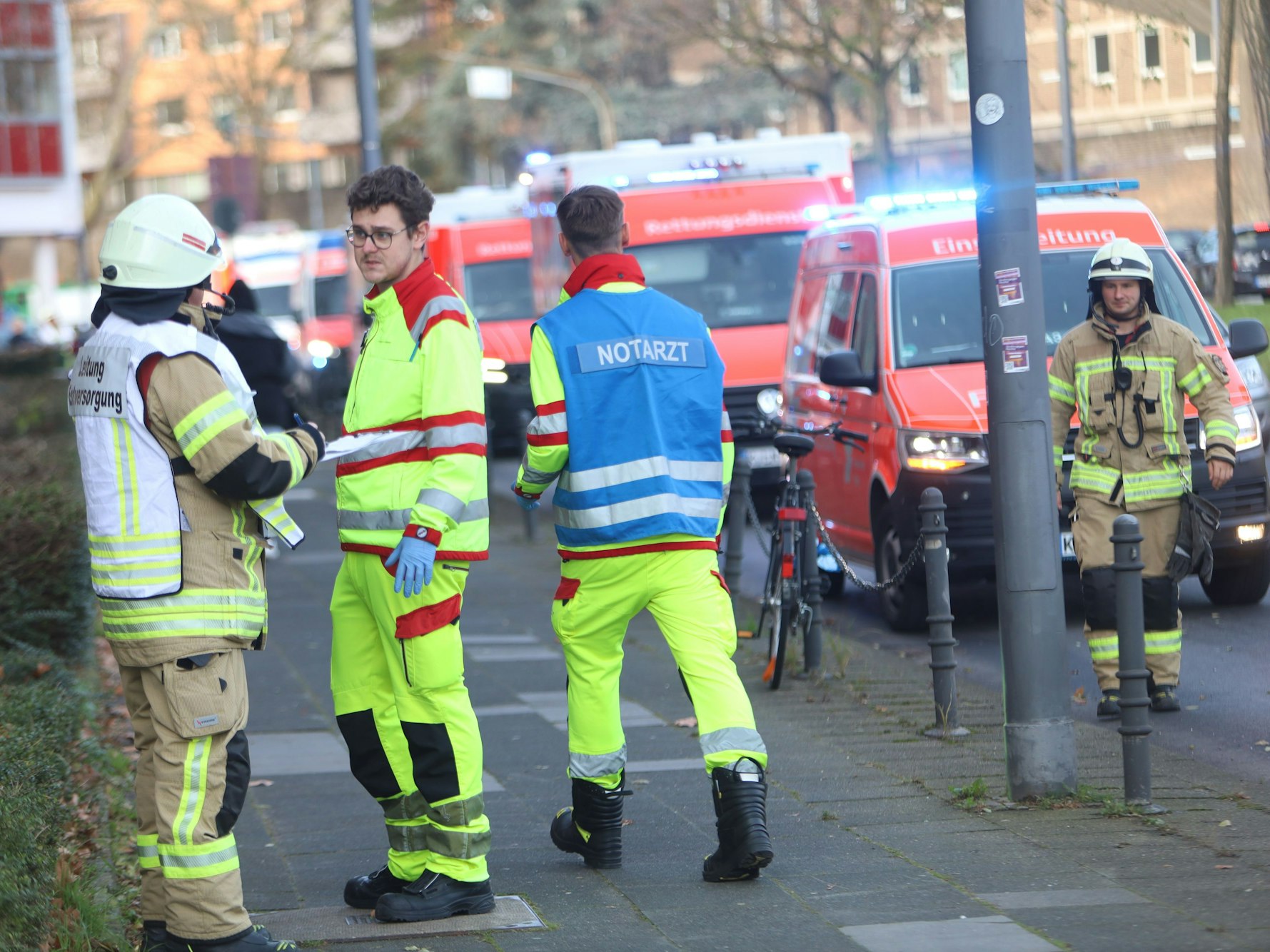 Einsatzfahrzeuge von Feuerwehr und Rettungsdienst stehen am Straßenrand, auf dem Gehweg befinden sich Einsatzkräfte, darunter ein Notarzt.