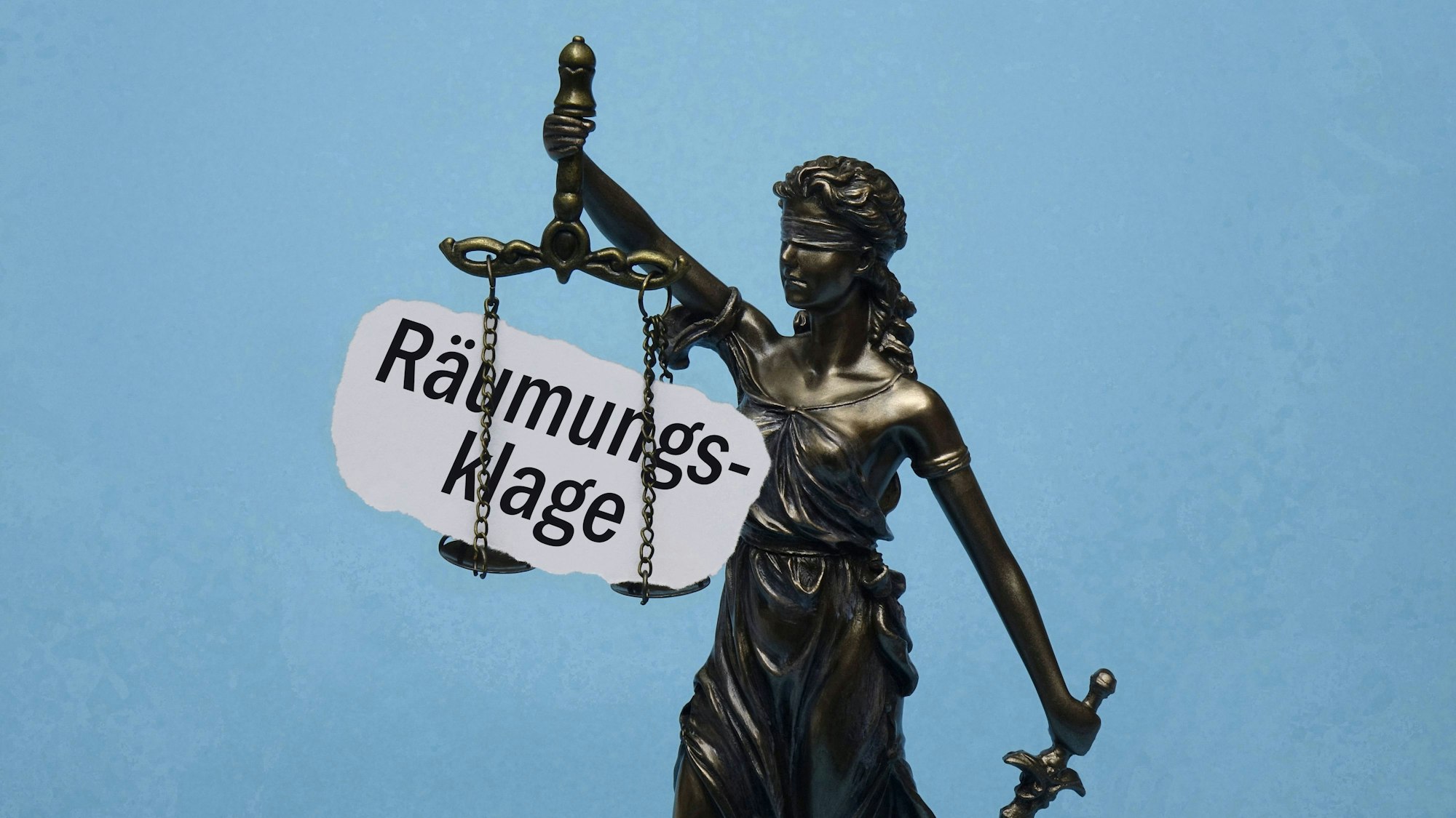 Justitia-Statue mit Zettel "Räumungsklage" an der Waage vor blauem Hintergrund