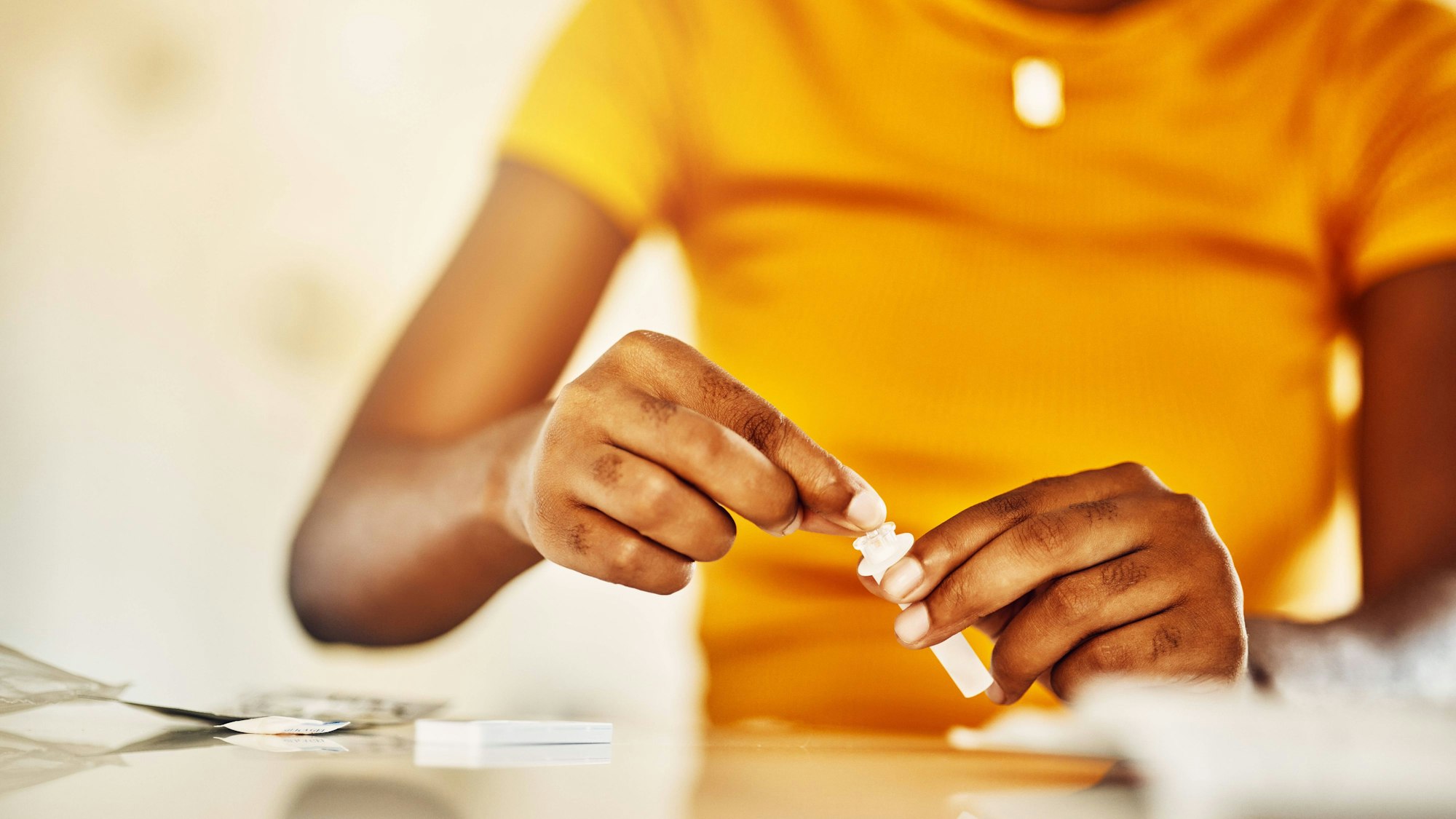Hände einer Person in gelbem Oberteil bereiten ein Aids-Test-Kit vor