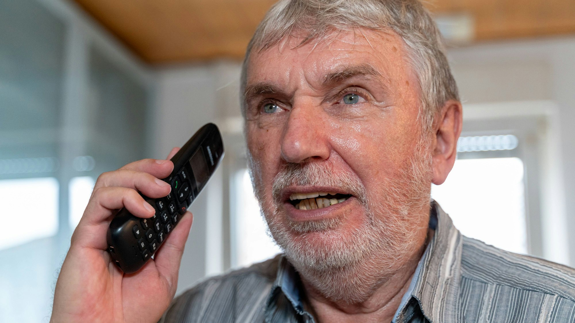 Nahaufnahme eines älteren Mannes mit Bart, der mit einem Telefon spricht