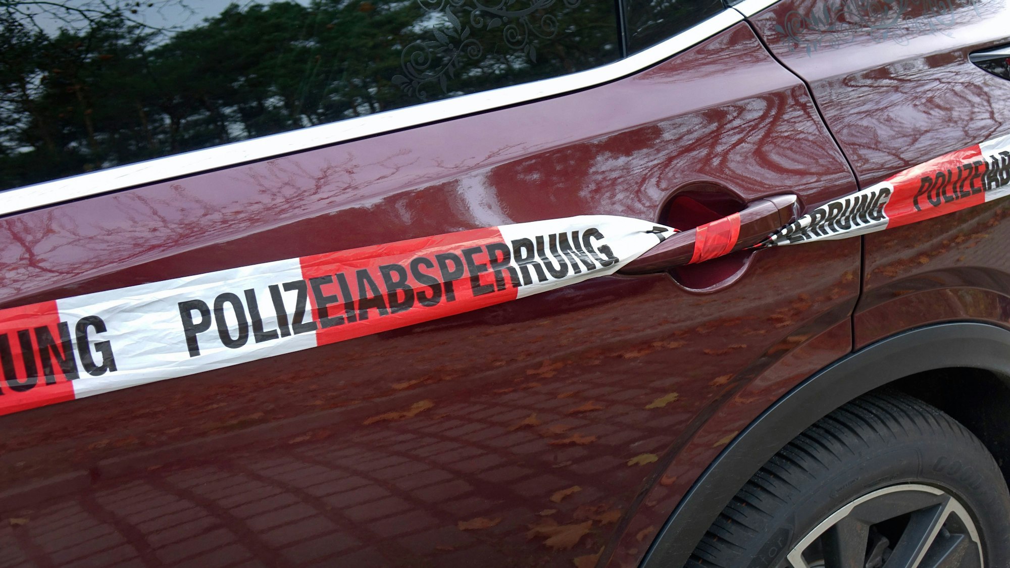 Polizei Absperrband an der Tür eines roten Autos, mit Reflexionen von Bäumen und Herbstlaub