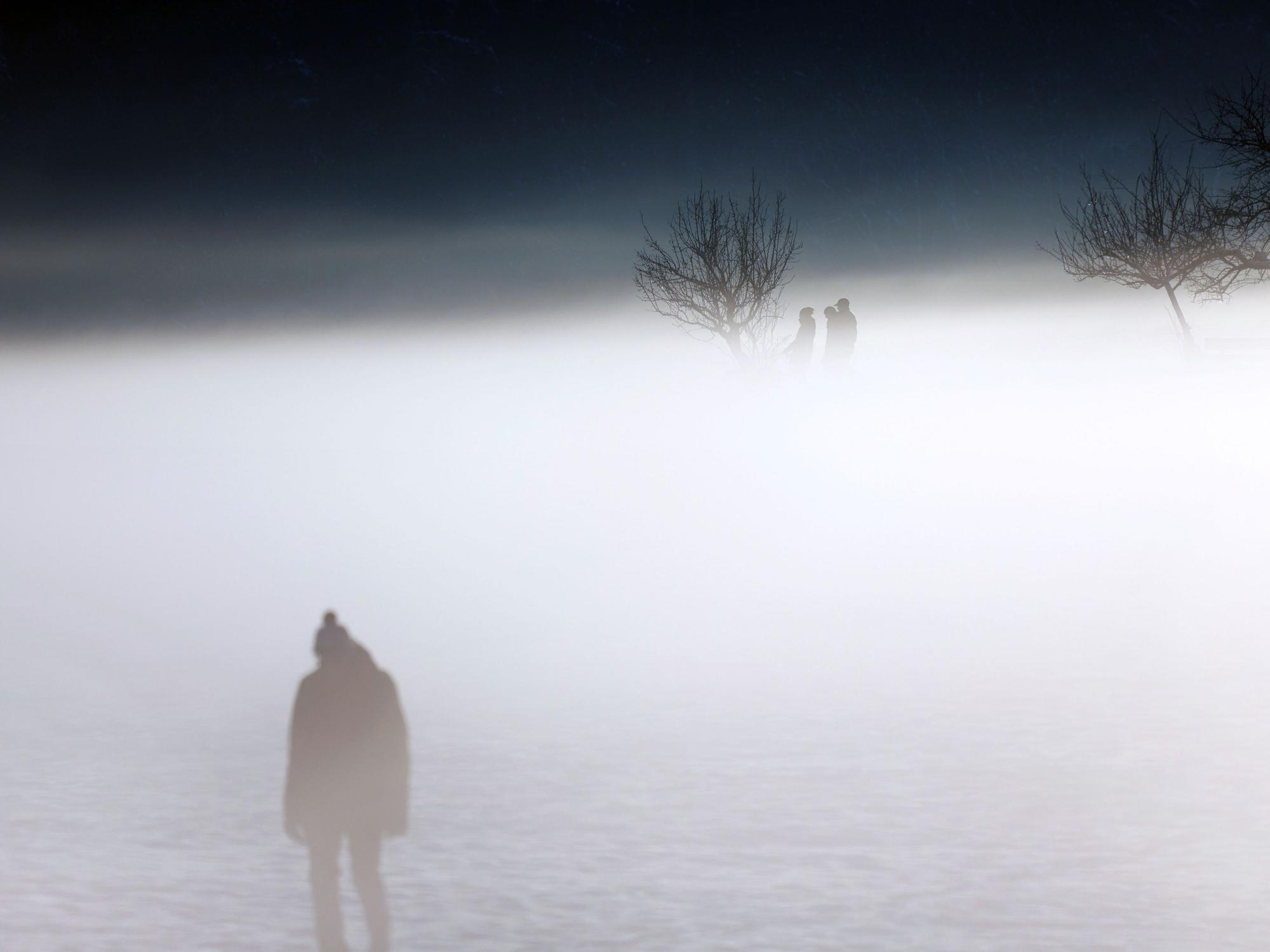 Menschen laufen durch dichten Nebel in winterlicher Landschaft.