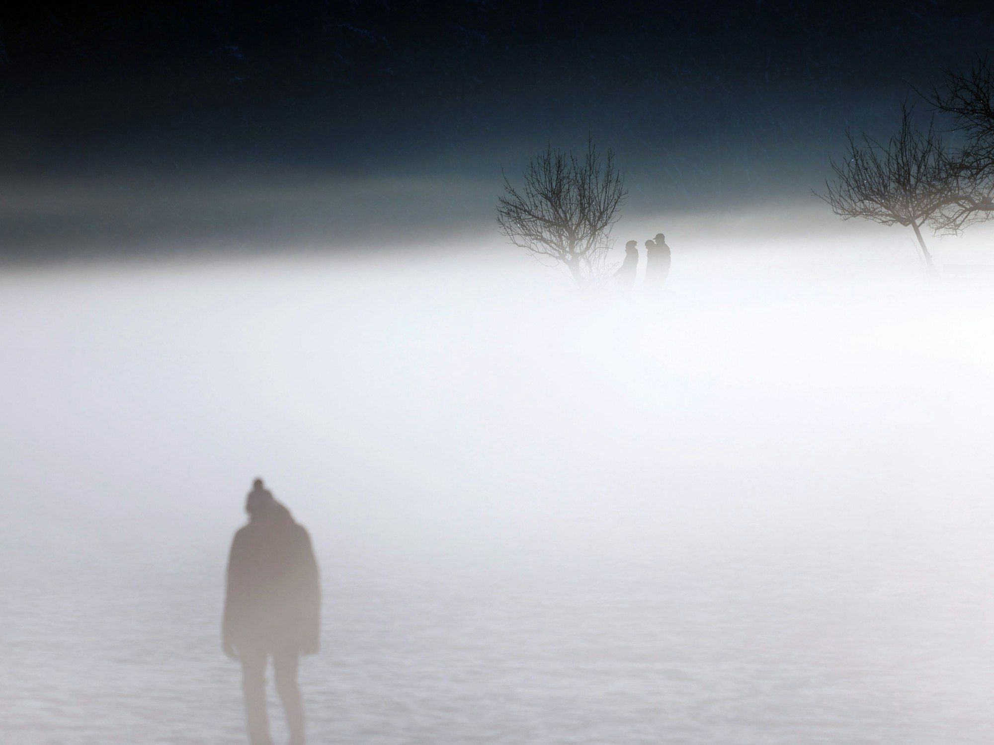 Menschen laufen durch dichten Nebel in winterlicher Landschaft.