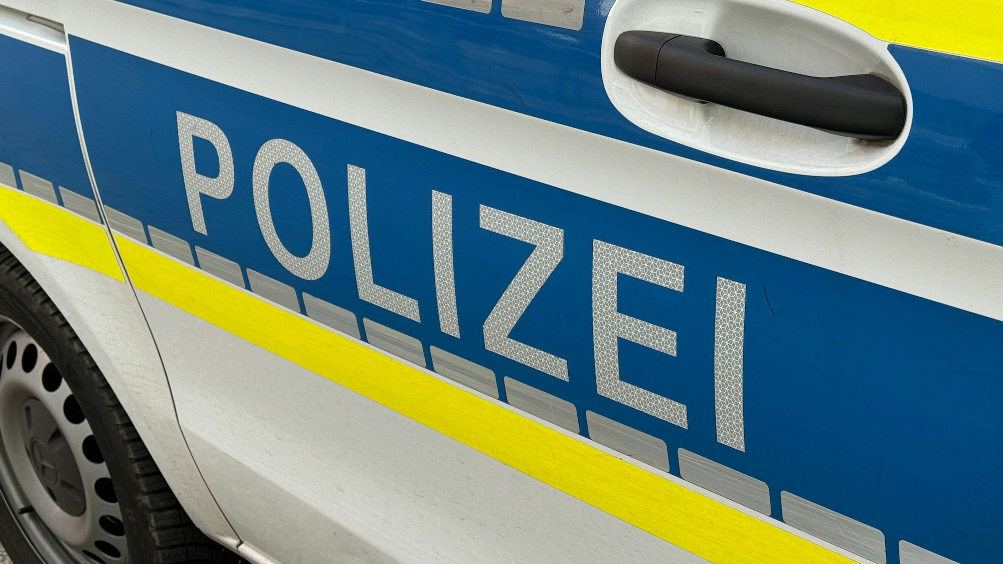 Seitenansicht eines Polizeiautos mit blau-gelb-weißem Design und dem Schriftzug "POLIZEI"