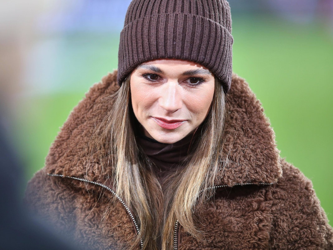 Jana Wosnitza in brauner Mütze und Teddyfelljacke blickt nach unten, unscharfer Hintergrund