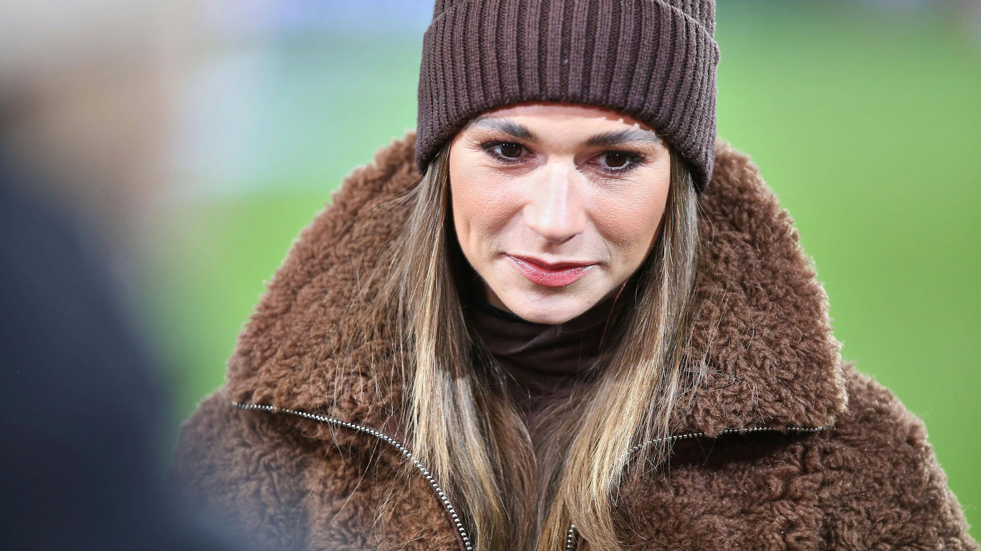 Jana Wosnitza in brauner Mütze und Teddyfelljacke blickt nach unten, unscharfer Hintergrund