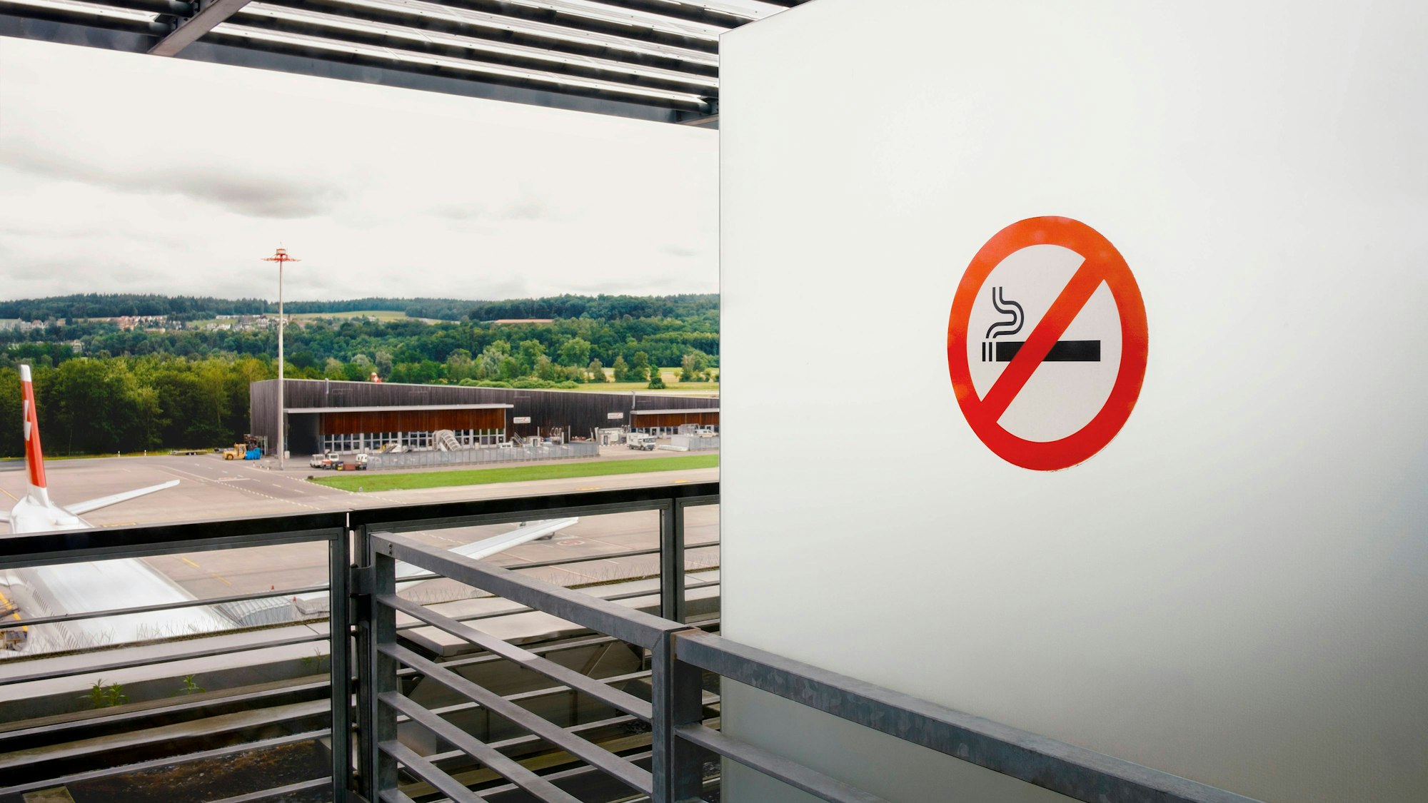 Kein Rauchen: Blick auf Flughafengelände mit Flugzeug, Gebäuden und grüner Landschaft
