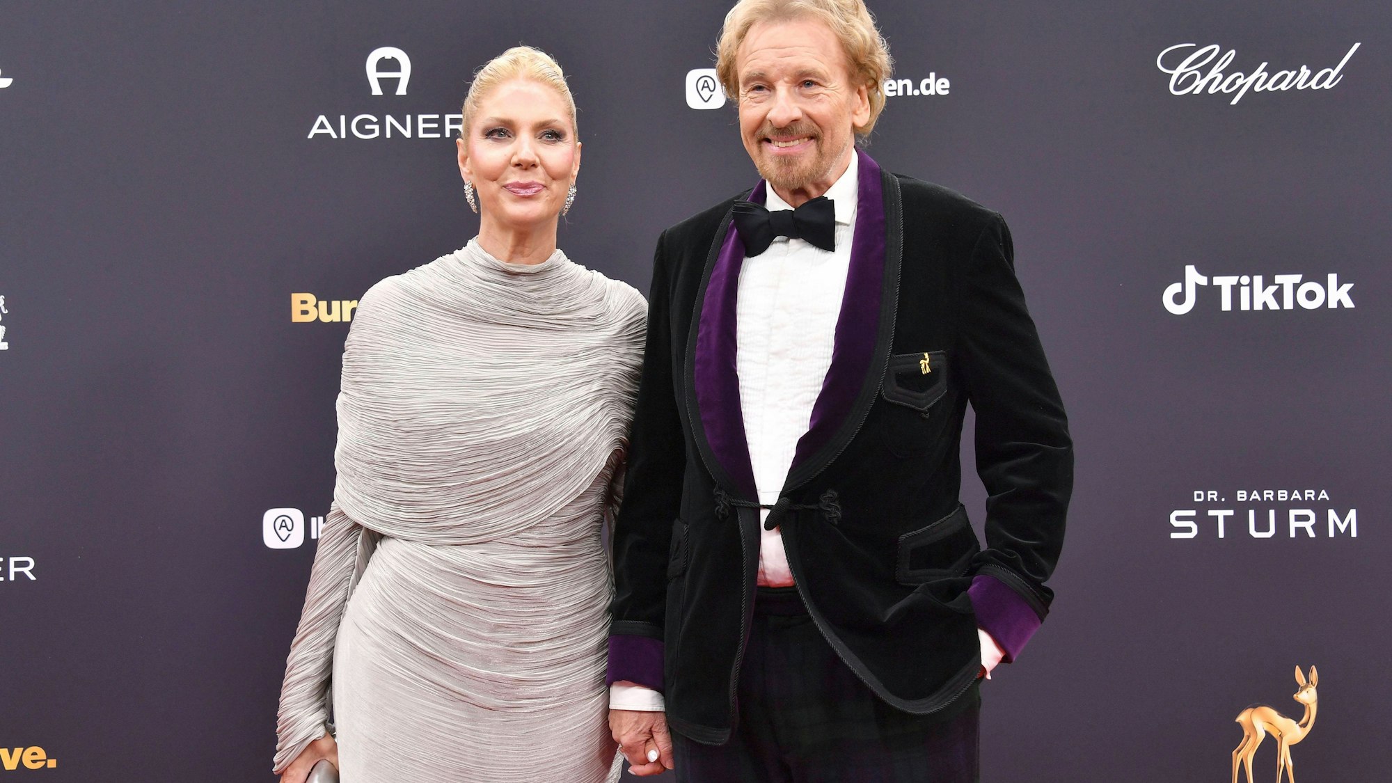 Thomas Gottschalk und Karina Mroß lächeln, Händchen haltend auf dem roten Teppich