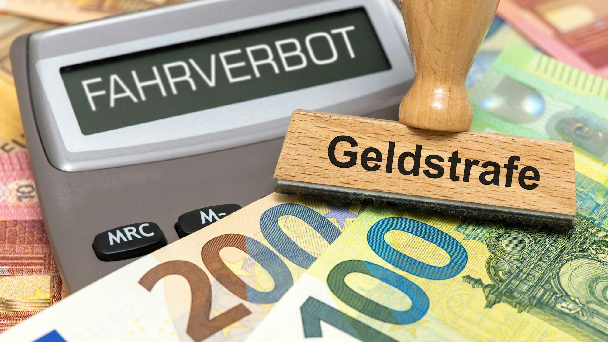 Ein Taschenrechner mit der Aufschrift "Fahrverbot", ein "Geldstrafe"-Stempel und Euro-Banknoten
