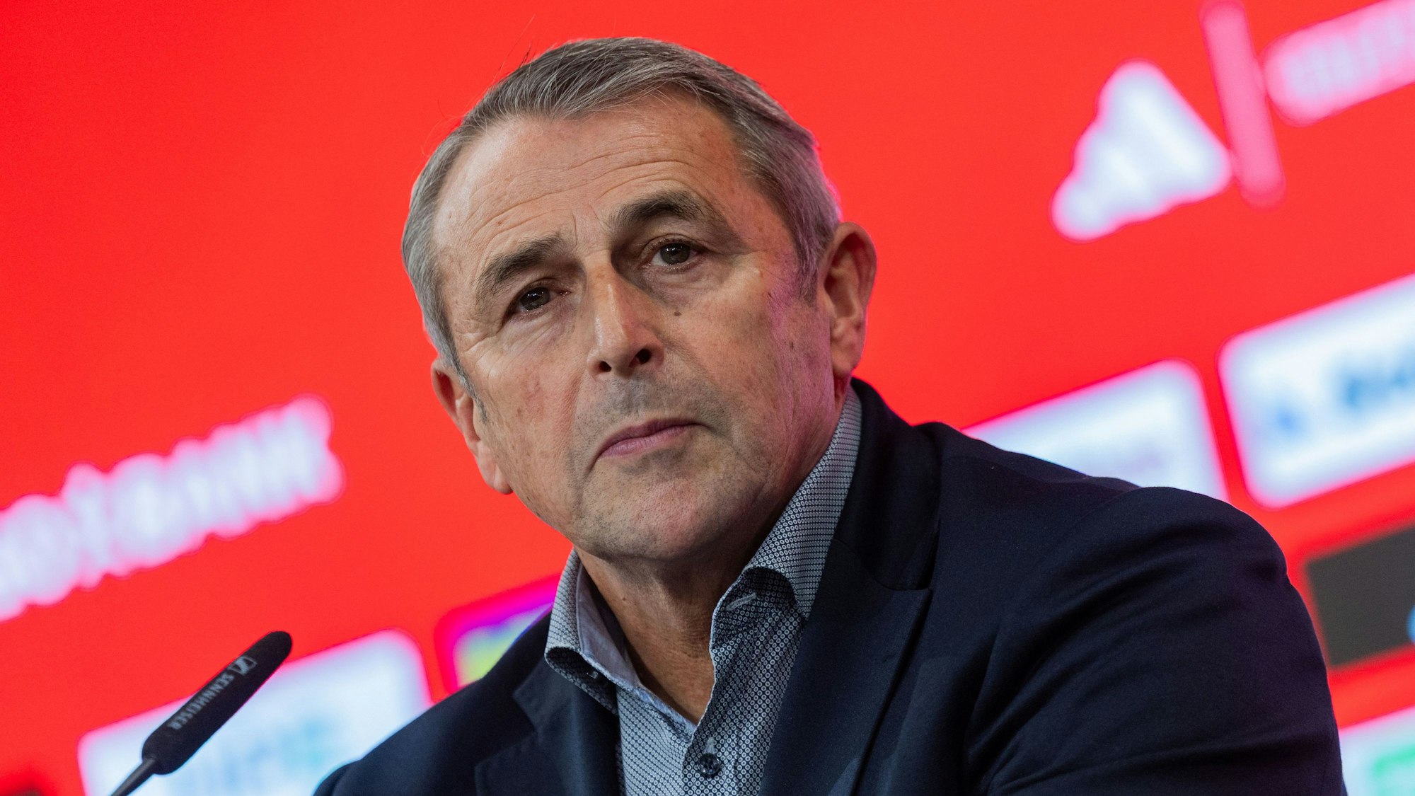 Klaus Allofs sitzt bei einer Pressekonferenz vor einem Mikrofon.