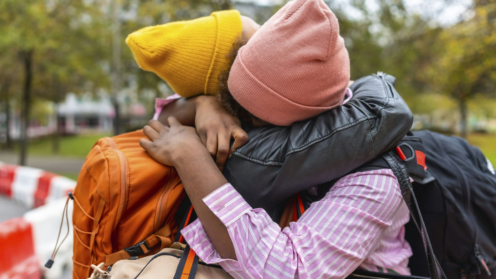 Zwei Personen umarmen sich mit Mützen und Taschen
