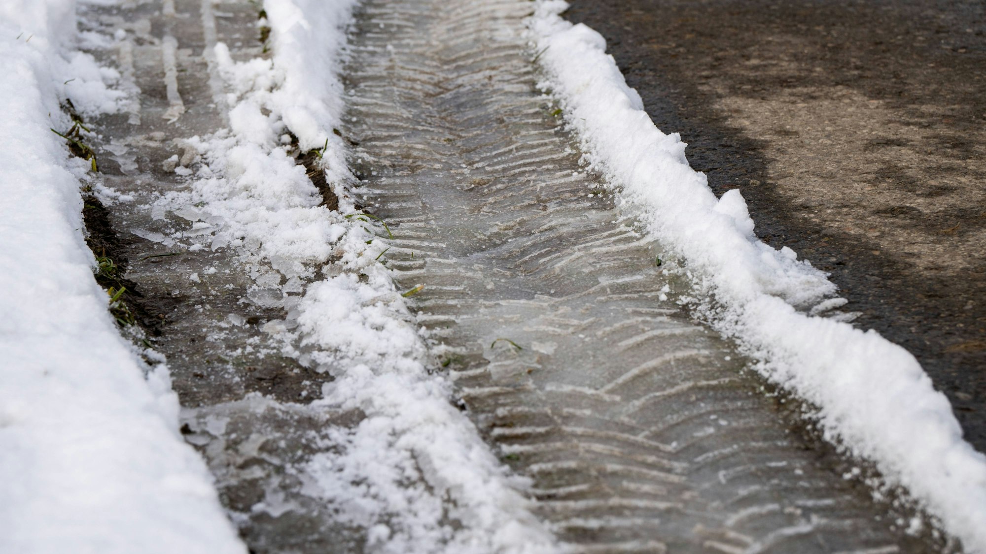 Reifenspuren in Glatteis und Schnee am Straßenrand