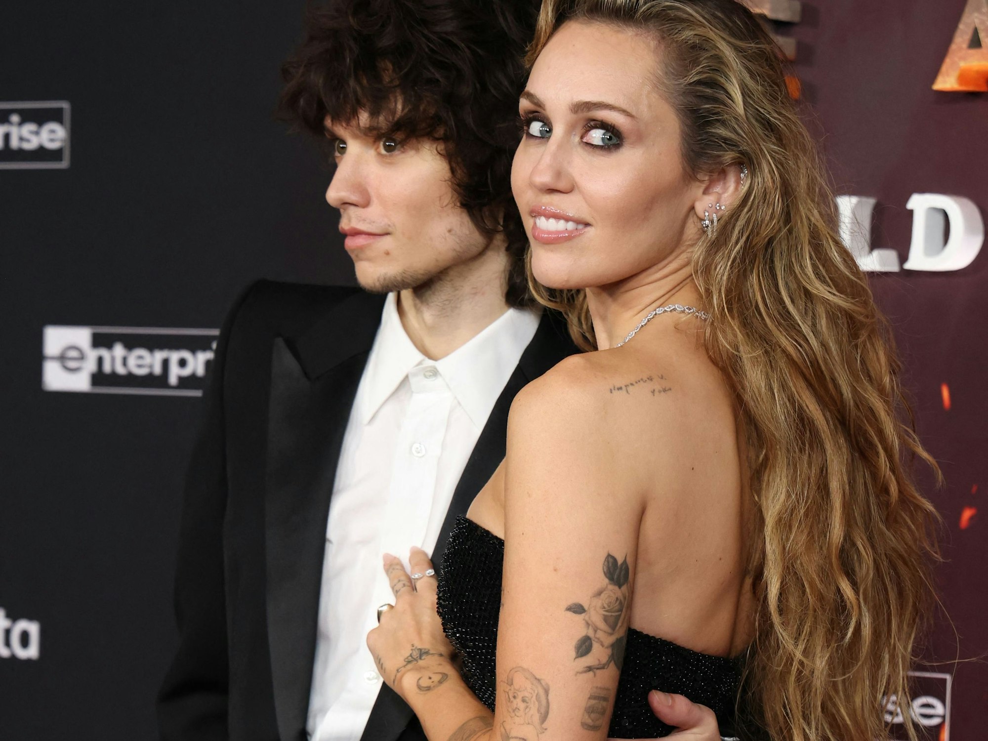 Ein Paar in Abendkleidung posiert vor einer Wand.