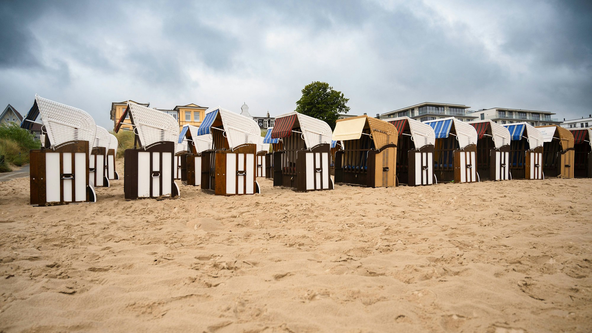 Sandstrand mit Strandkörben und Gebäuden unter bewölktem Himmel