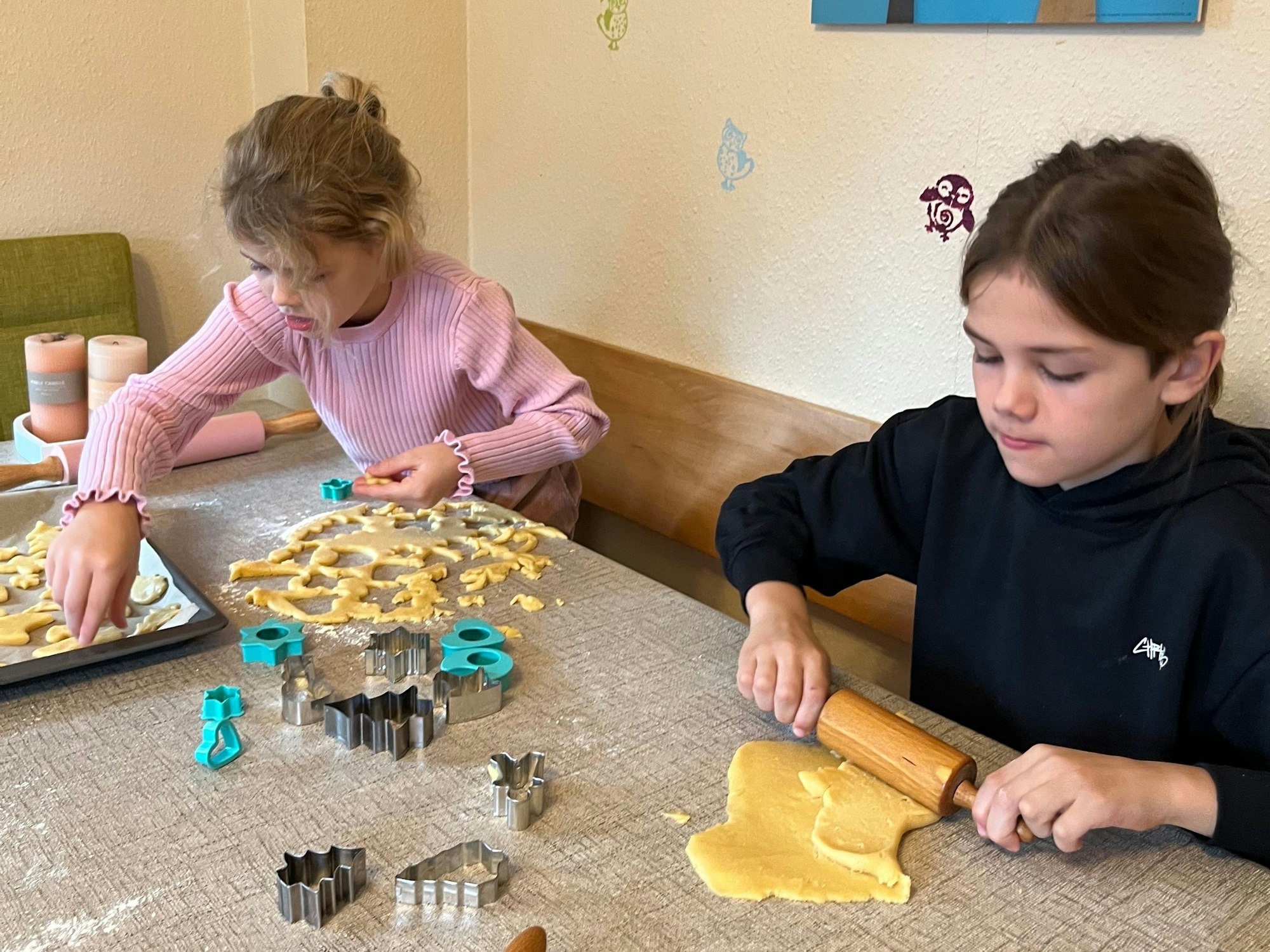 Zwei Mädchen rollen Plätzchenteig aus und stechen Weihnachtskekse aus