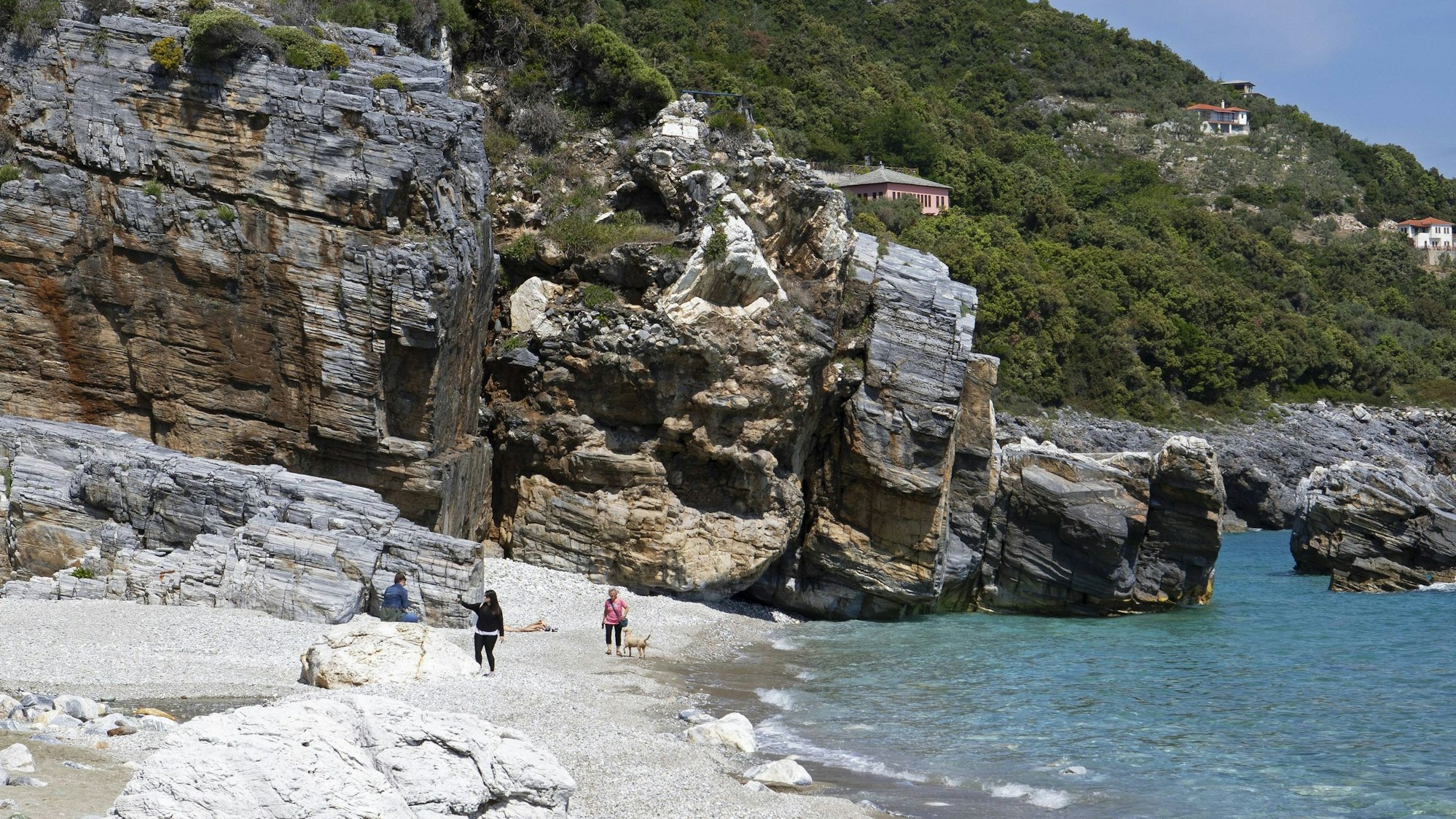 Milopotamos Strand mit Felsen, klarem türkisem Wasser, grünem Hügel und wenigen Menschen