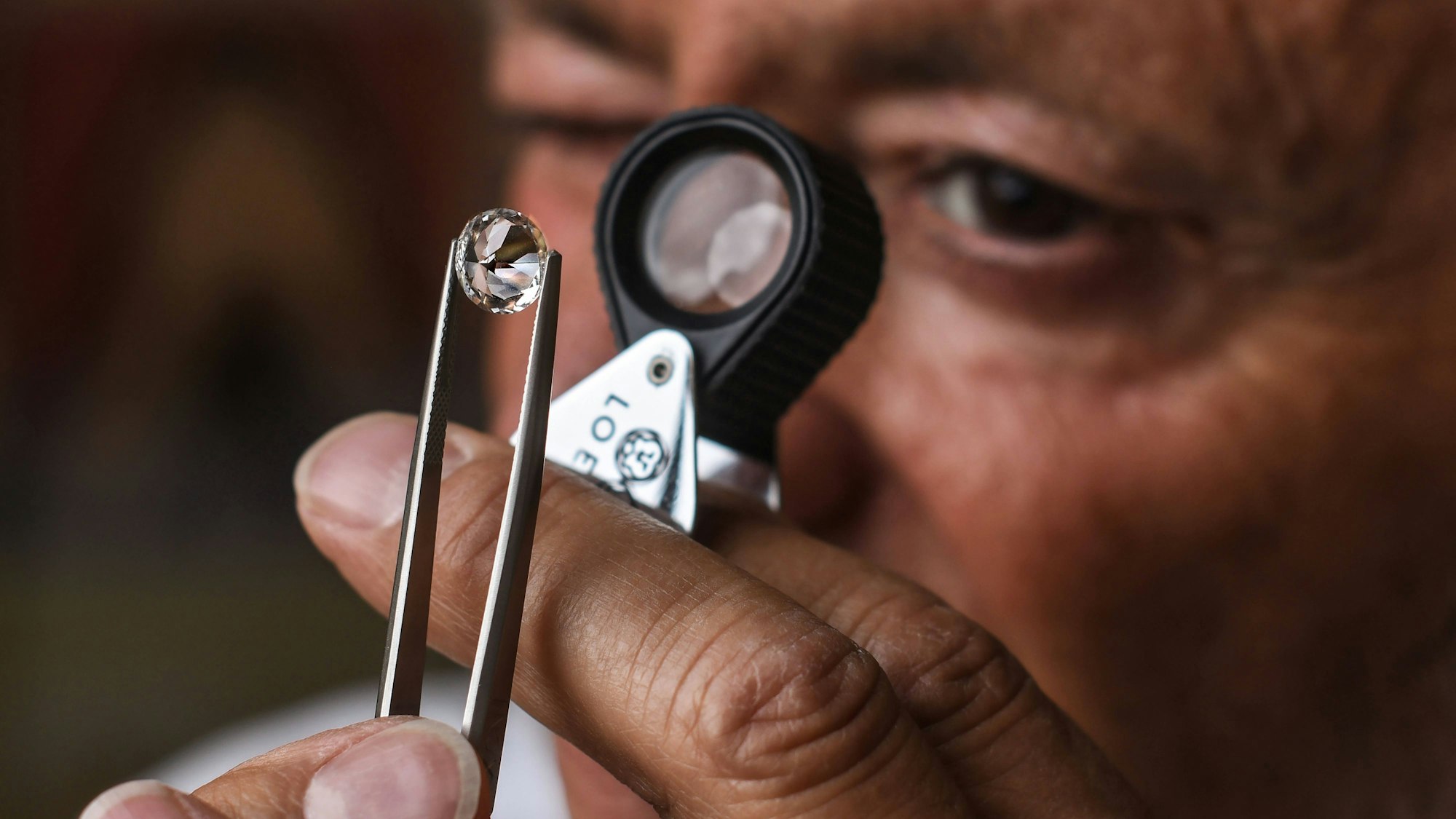 Ein Juwelier prüft einen Edelstein mit einer Lupe und Pinzette