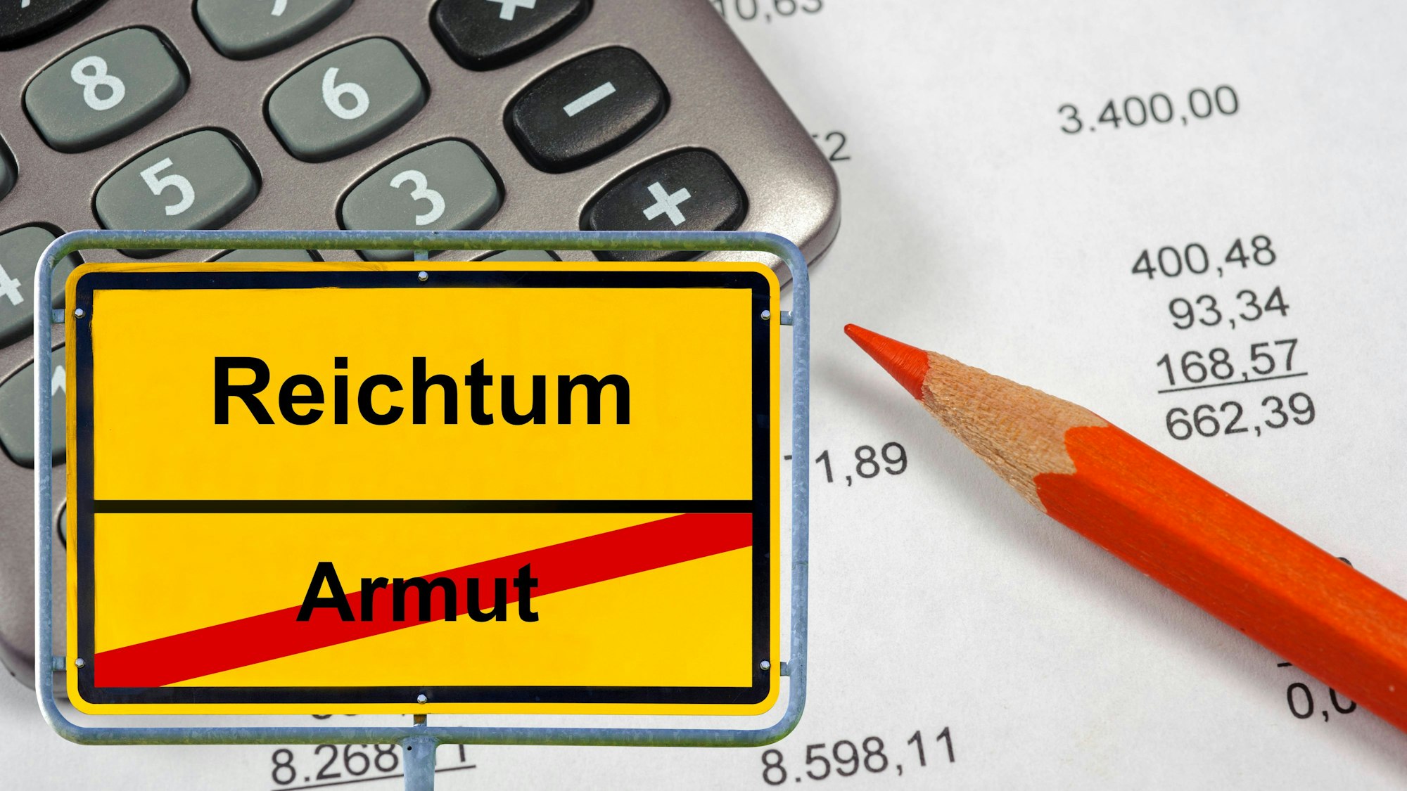 Gelber Wegweiser mit Reichtum und Armut, dahinter Taschenrechner, Bleistift und Finanzzahlen