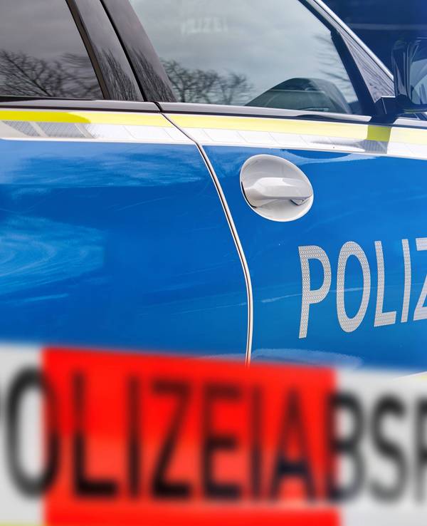 Polizeiauto mit 'POLIZEI'-Schriftzug und unscharfem rot-weißem Absperrband 'POLIZEIABSPERRUNG' im Vordergrund