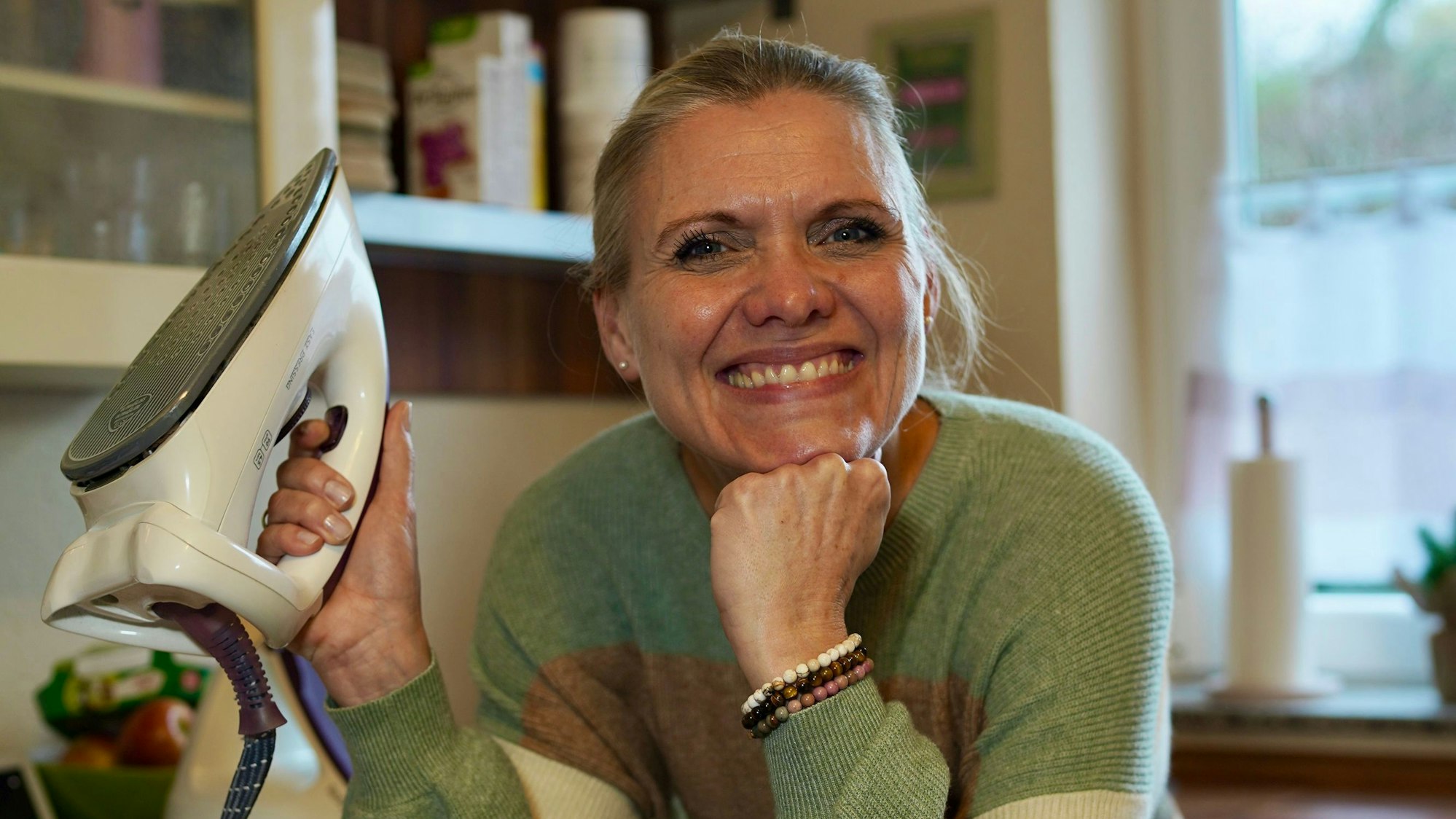 Eine Frau hält ein Bügeleisen und lacht in die Kamera