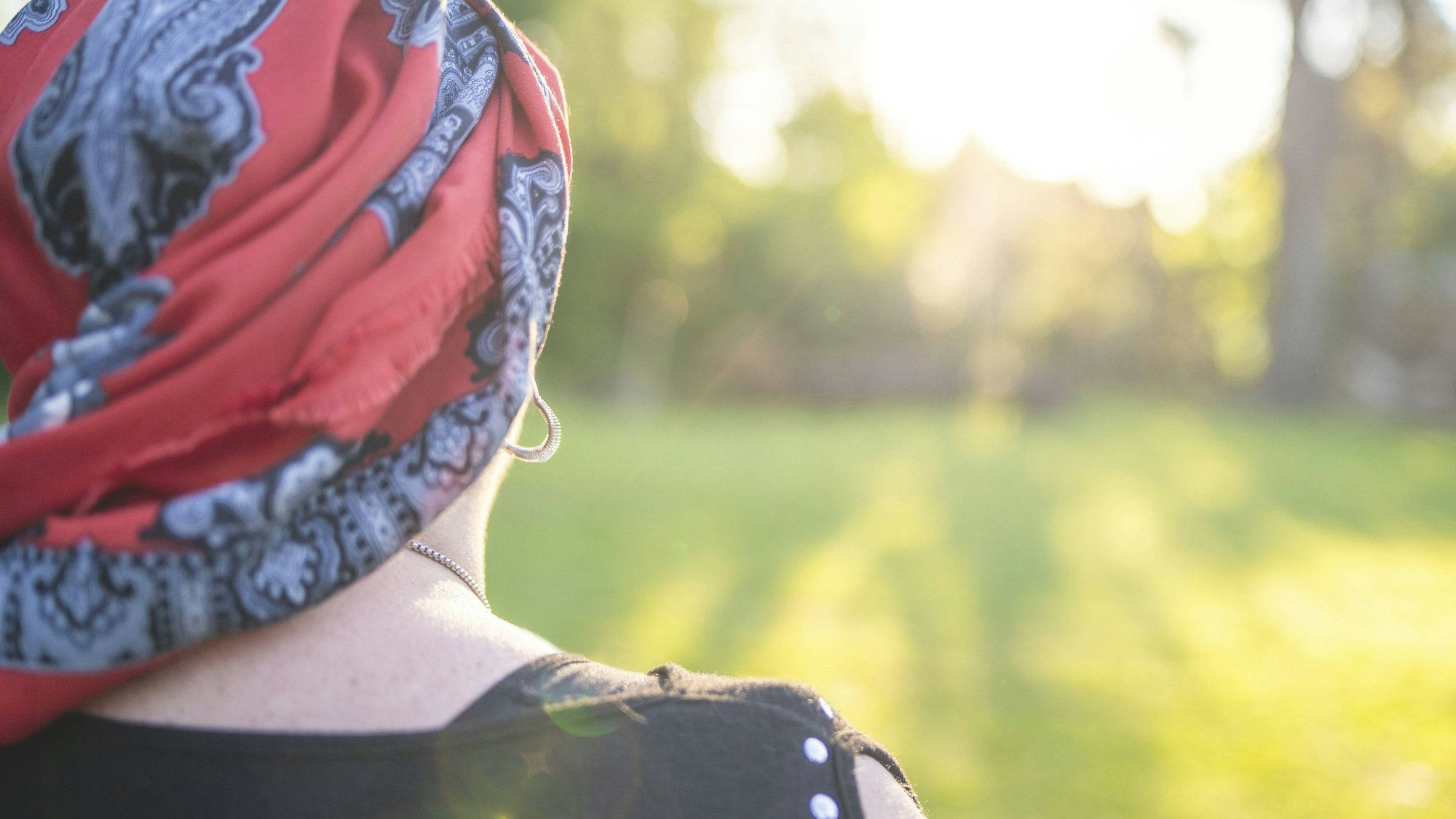 Eine Frau mit rotem, gemustertem Kopftuch blickt in die helle Natur