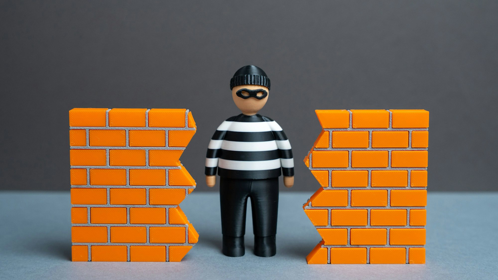 Eine Diebesfigur steht in einem Loch in einer zerbrochenen orangefarbenen Ziegelmauer