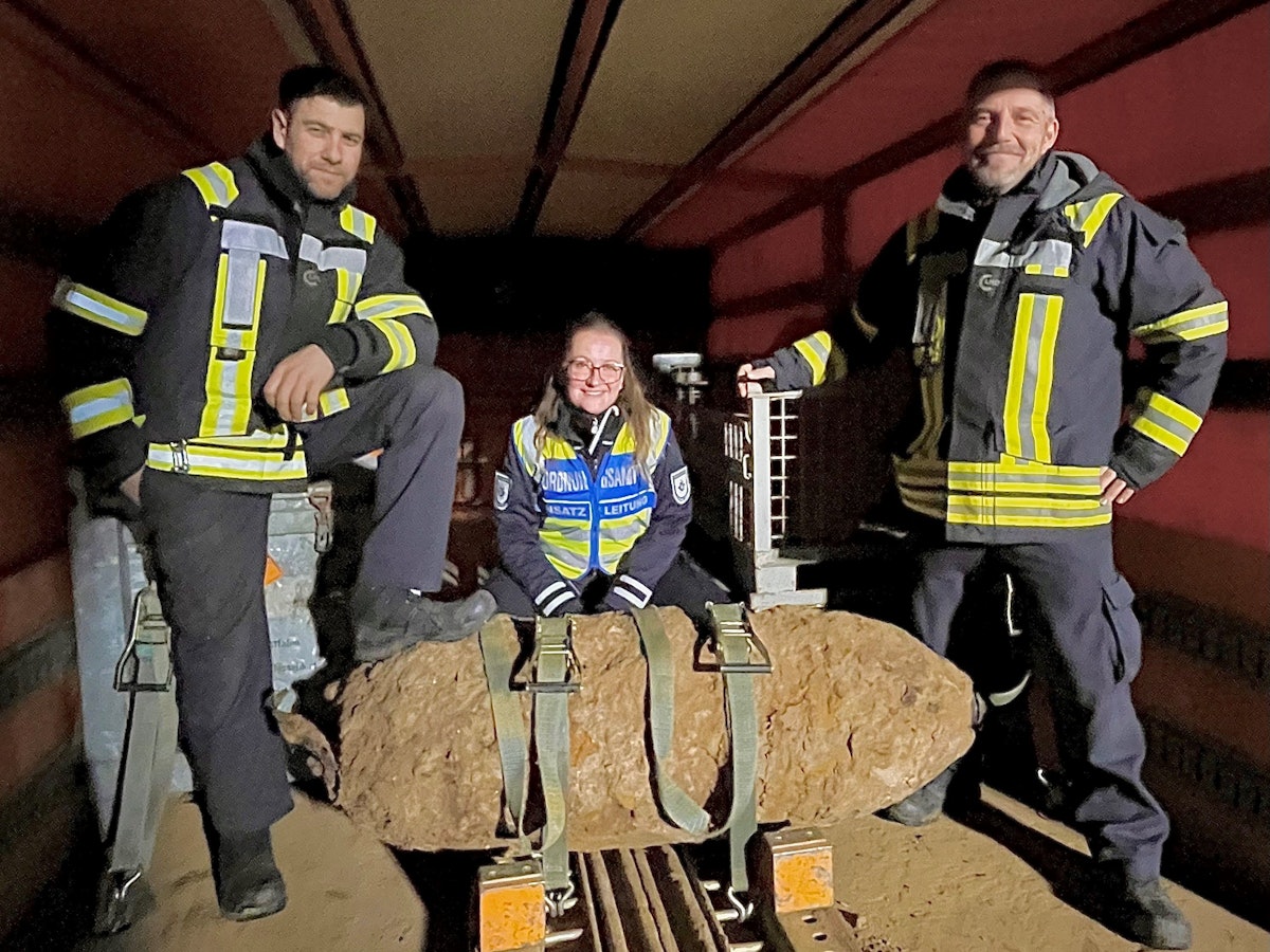 Zwei Männer und eine Frau posieren an einer entschärften Bombe.