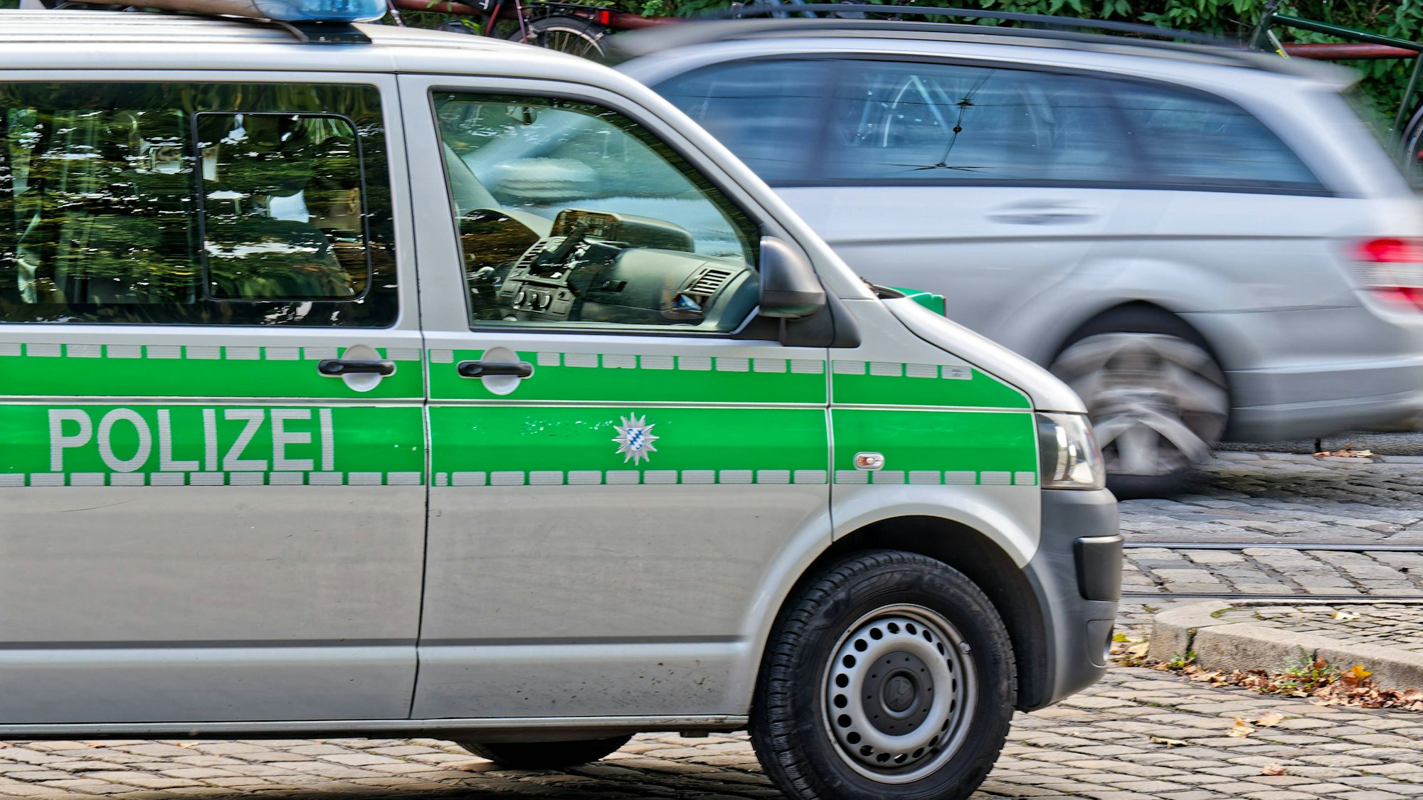 Polizeifahrzeug in München im Einsatz auf gepflasterter Straße, ein Auto fährt vorbei